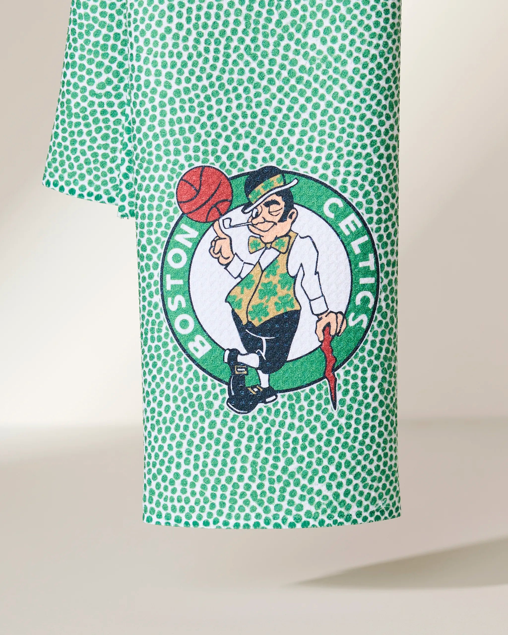 The Geometry Celtics Grip is a green towel with a dotted pattern featuring the Boston Celtics logo—a leprechaun spinning a basketball and leaning on a cane—set within a white circle with Boston Celtics text.