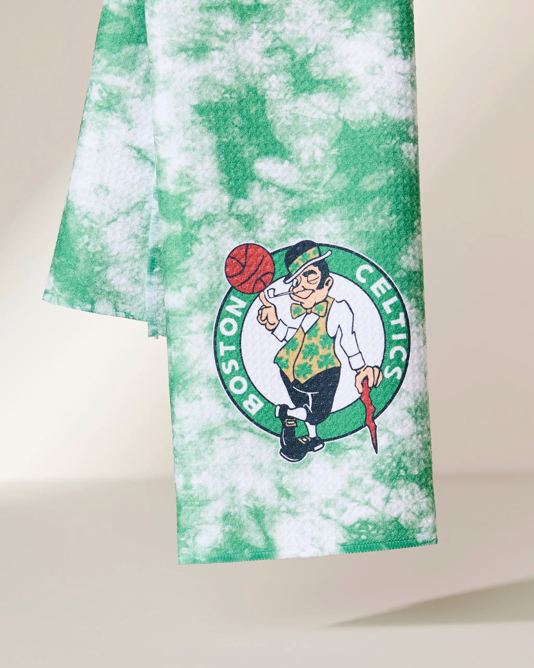 The Geometry Celtics Flash towel is green and white tie-dye and features the Boston Celtics logo with the team’s leprechaun mascot spinning a basketball.