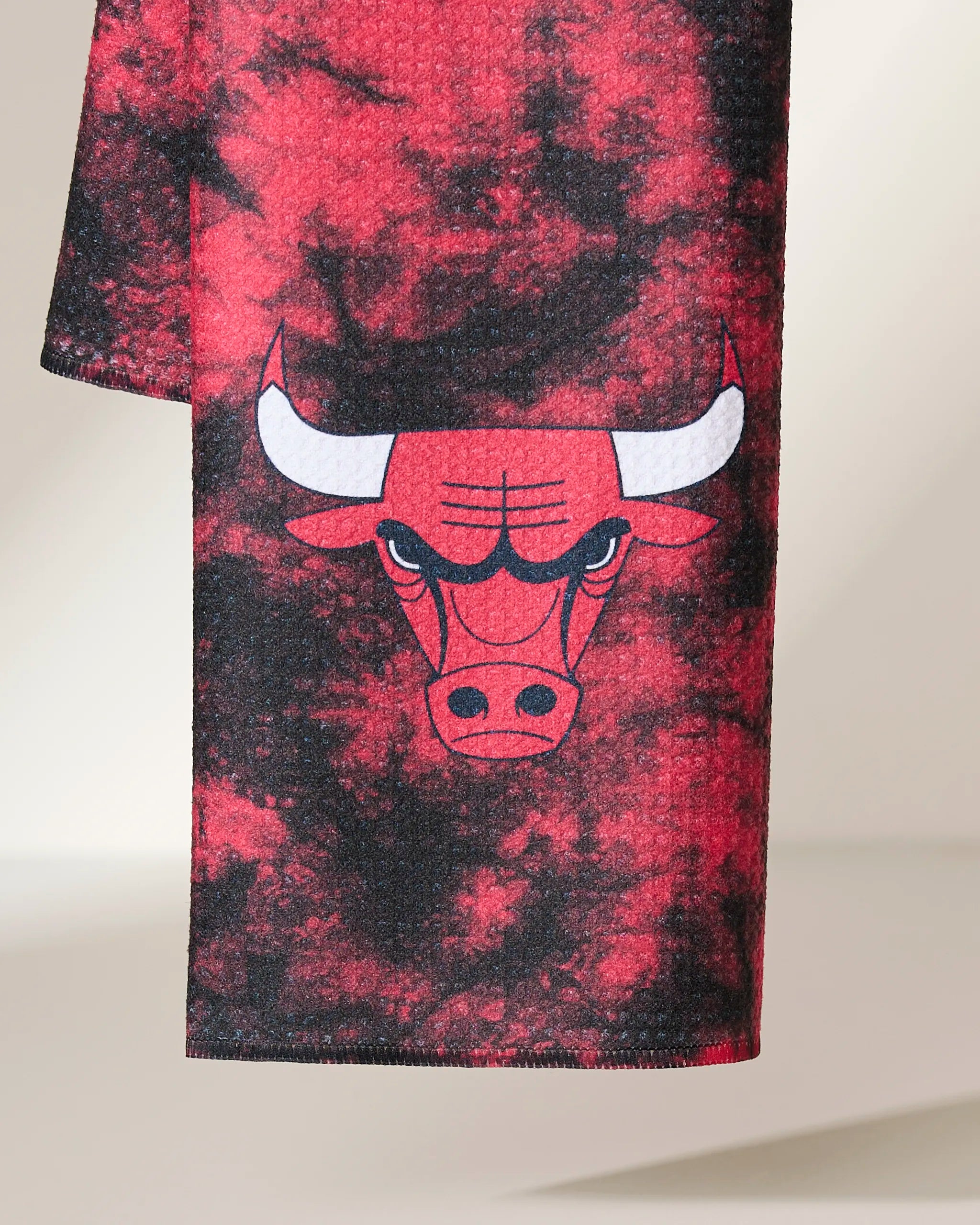 A close-up of Geometry’s Bulls Flash kitchen towel, showcasing a red and black tie-dye design with the iconic Chicago Bulls bulls face and horns logo, set against a neutral background.