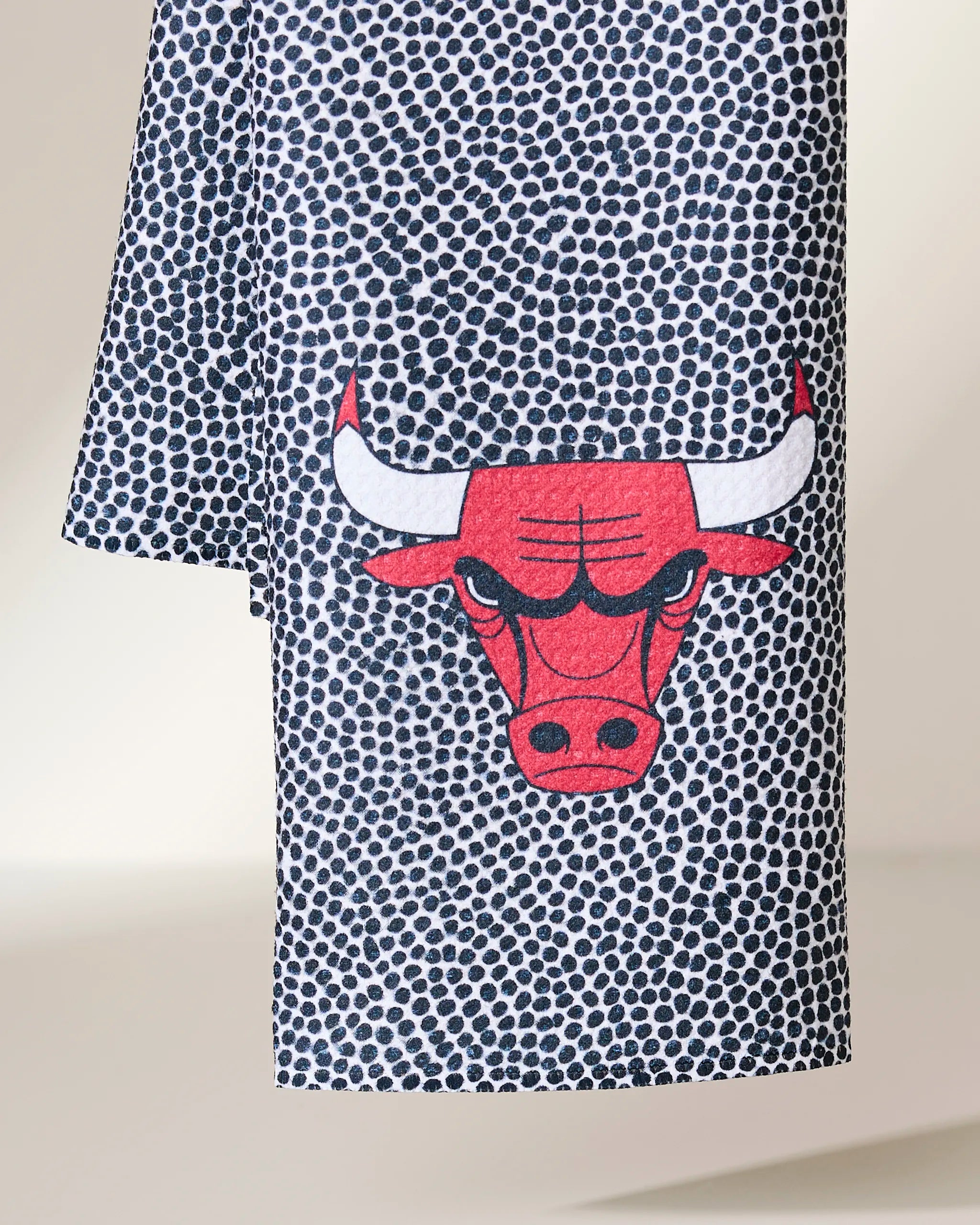The Geometry Bulls Grip is a quick-drying tea towel with a pattern of small dark dots on white, featuring the red Chicago Bulls logo with a fierce bull’s face and white horns at the center.