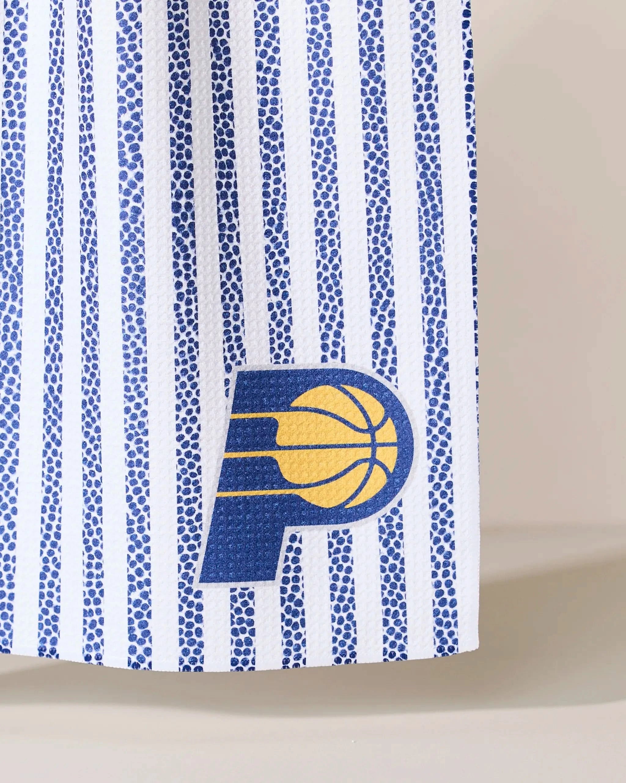 A close-up of Geometrys Pacers Grip Stripe fabric shows blue and white vertical stripes with the Indiana Pacers logo—a blue P and yellow basketball—printed near the bottom.