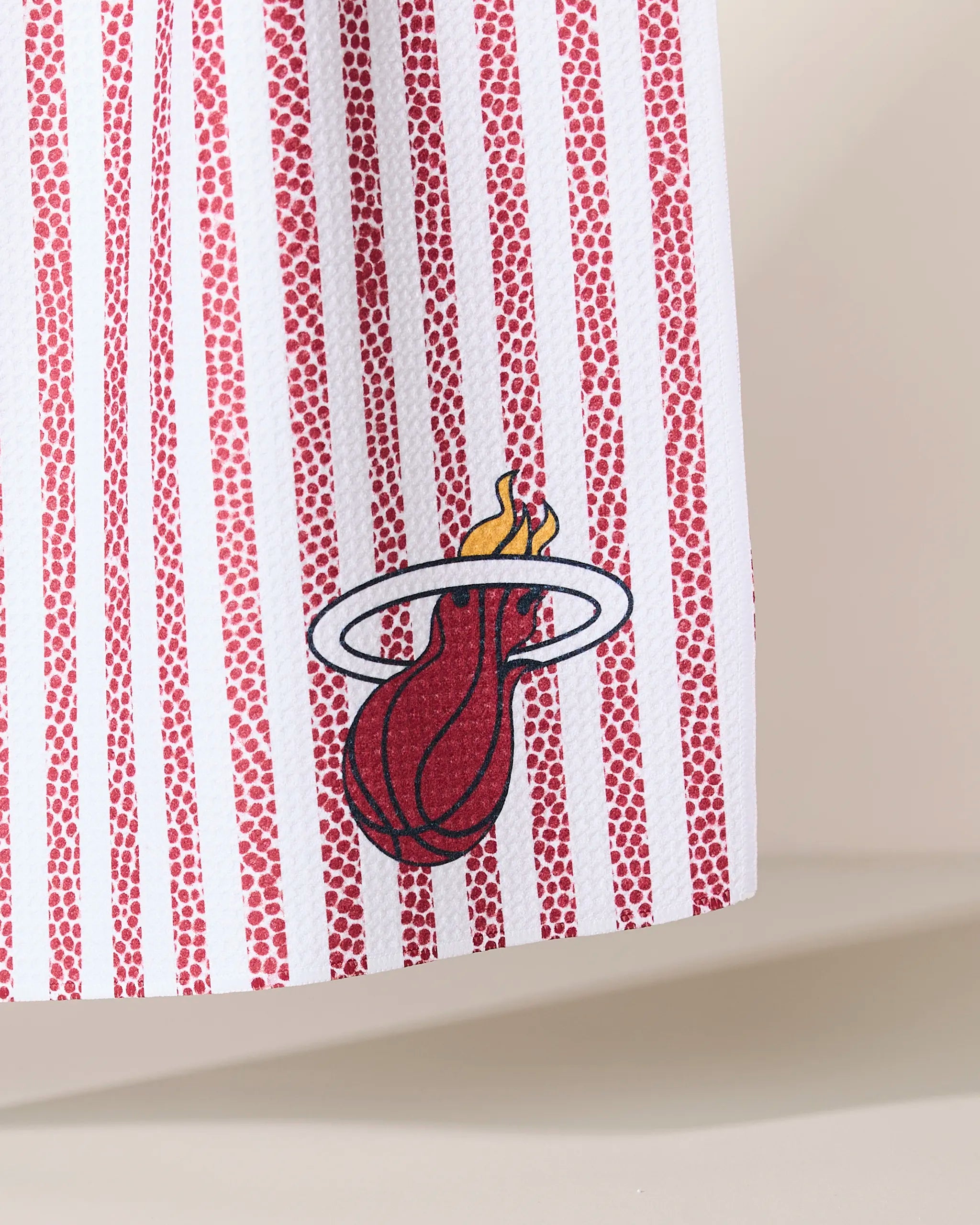 A close-up of the Geometry Heat Grip Stripe Red fabric, showcasing vertical red and white stripes and the Miami Heat logo with a flaming basketball passing through a hoop.