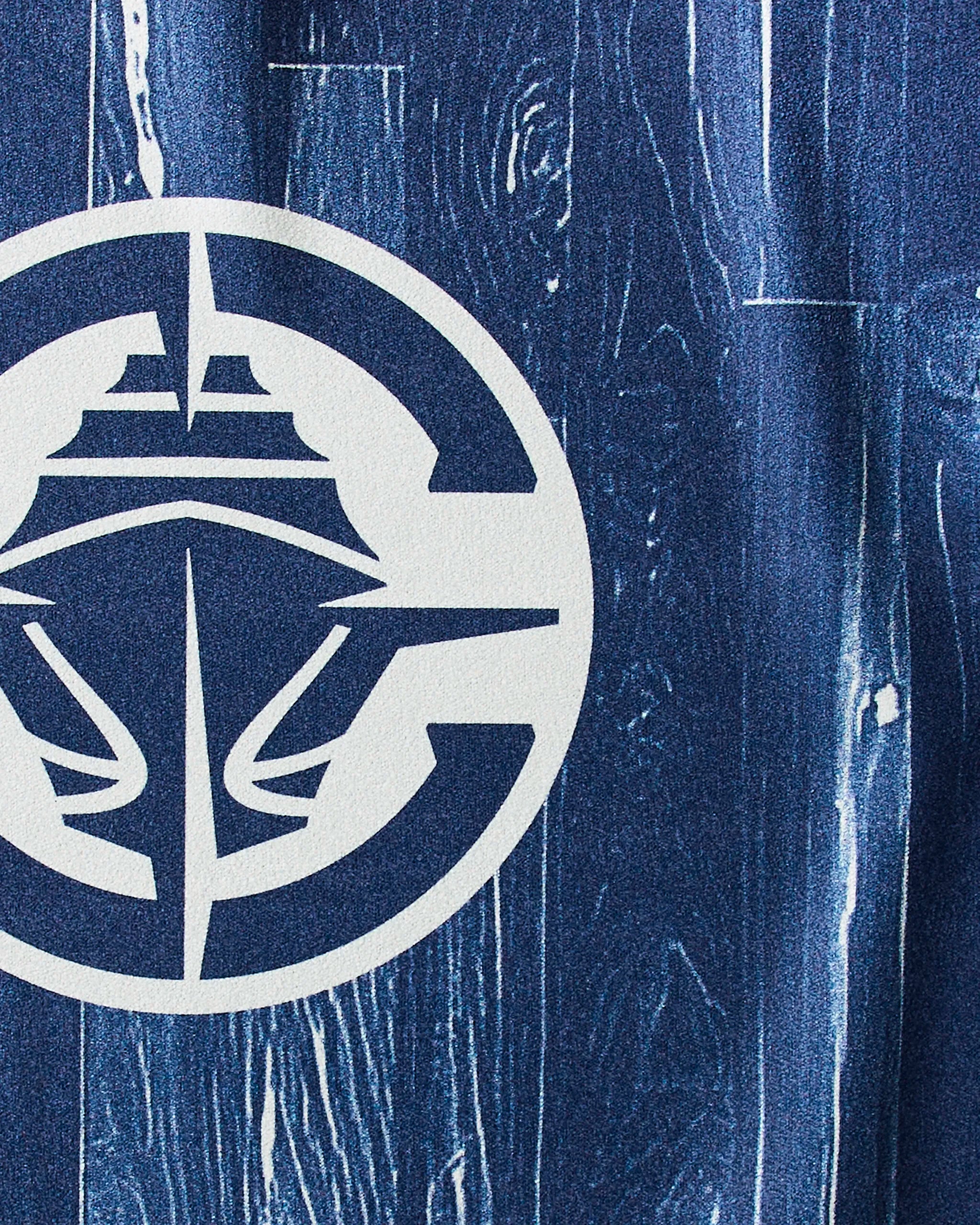 A white stylized ship logo inside a circle on textured dark blue, wood grain-like background—ideal inspiration for a Clippers Zone by Geometry sustainable gym or quick-drying workout towel design.