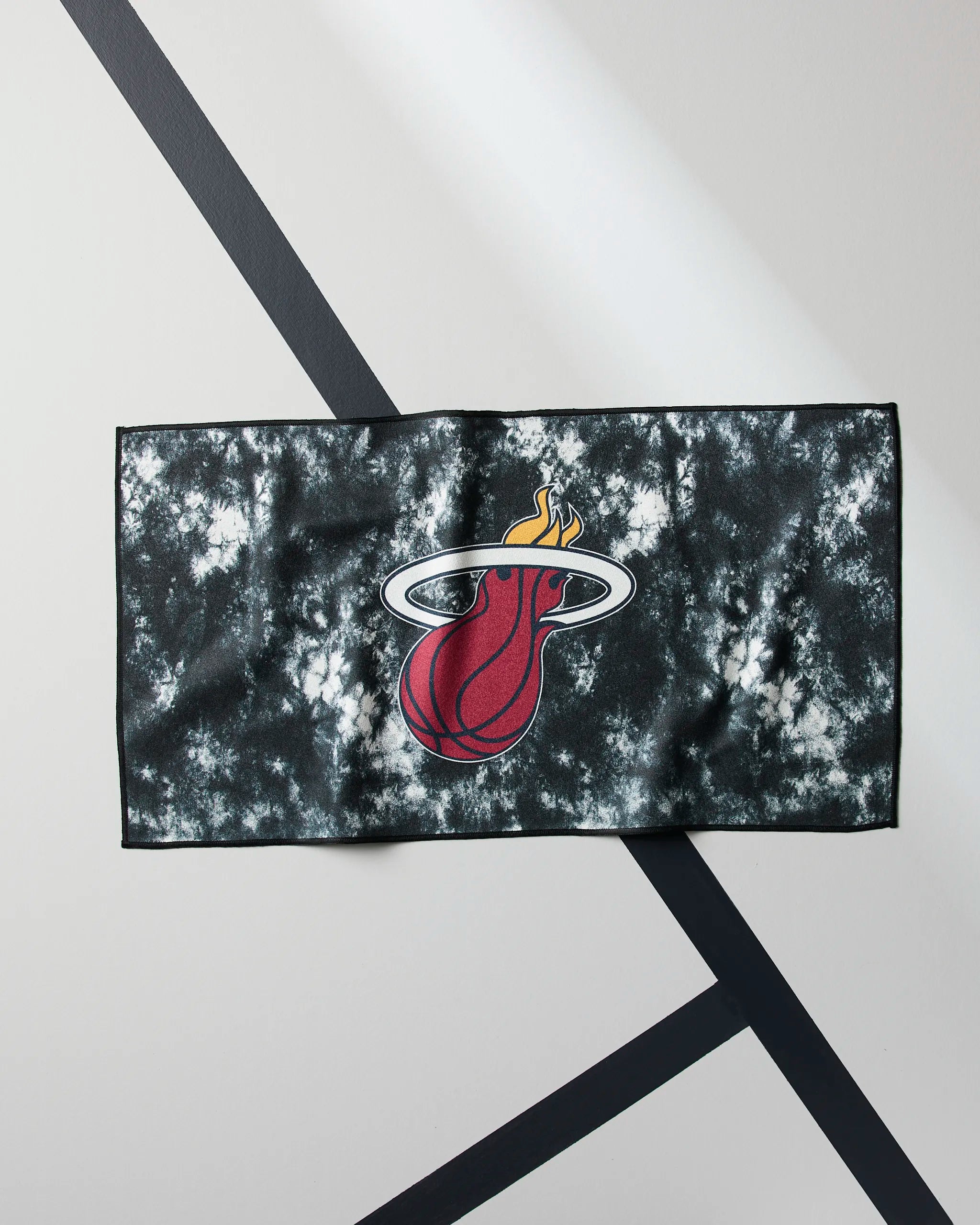 The Geometry Heat Flash is a black and white quick-drying gym towel featuring the Miami Heat flaming basketball logo, laid flat on a geometric background.