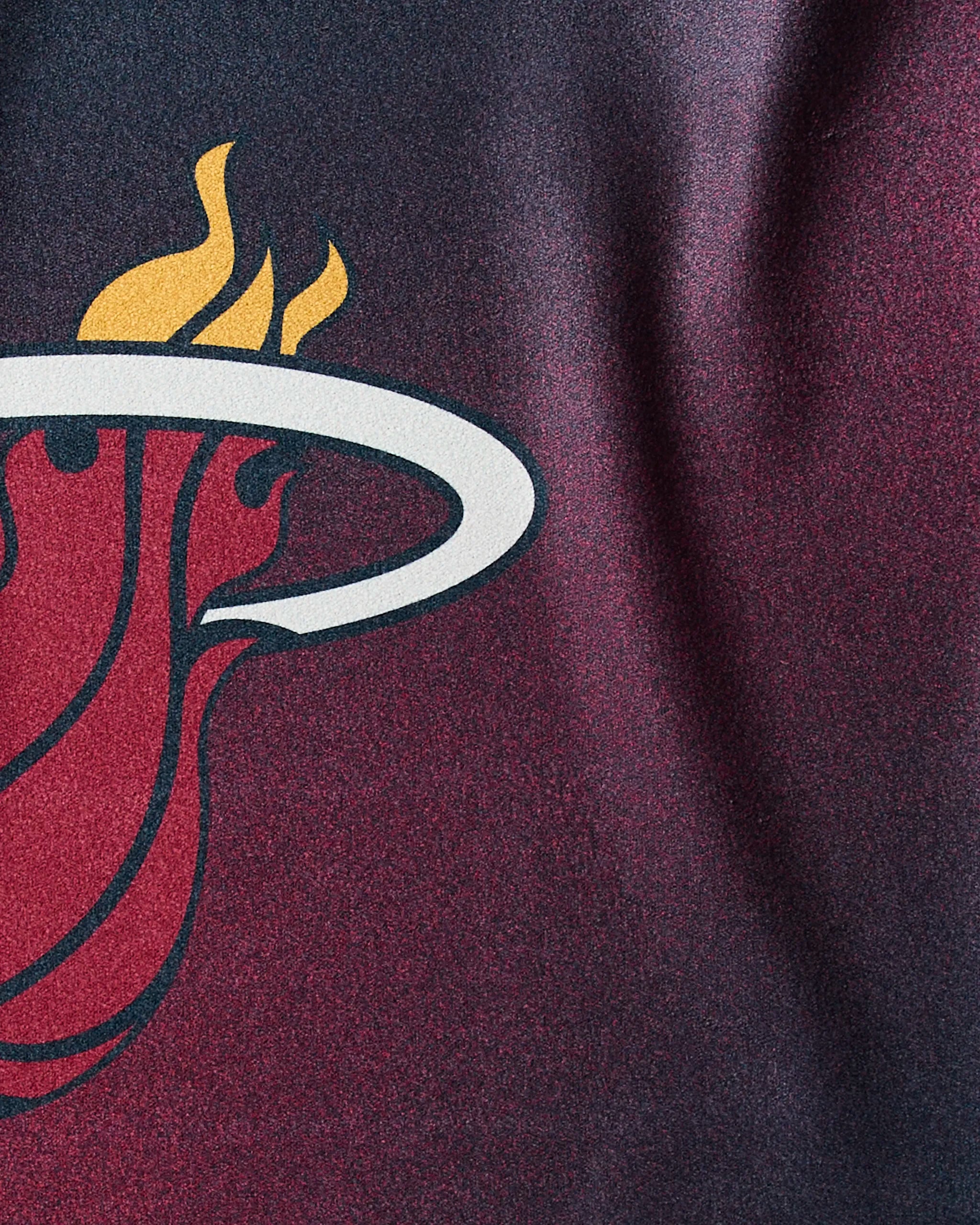 Close-up of the Geometry "Heat Fade" workout towel featuring the Miami Heat logo, with a flaming basketball through a white hoop on dark red and black quick-drying fabric.