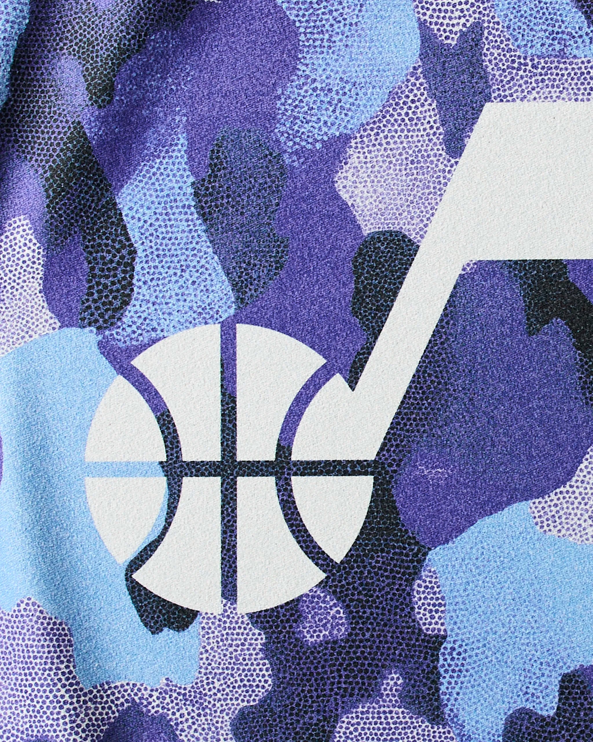 The Geometry Jazz Camo workout towel features a white Utah Jazz logo with a basketball and musical note on purple and blue camo Geoweave fabric—a sustainable, stylish addition to any NBA fitness towel collection.