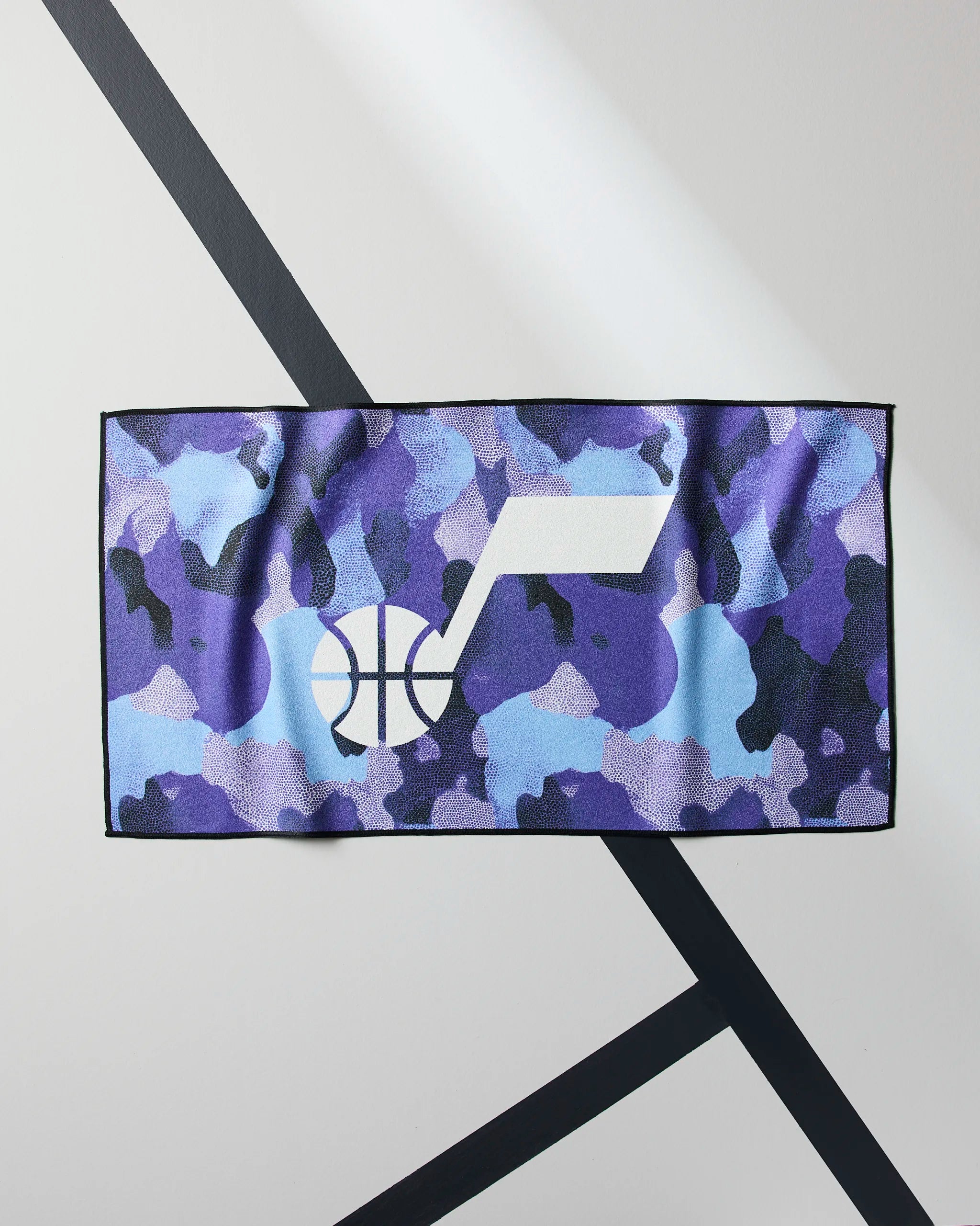 The Jazz Camo by Geometry is a rectangular NBA fitness towel with a blue and purple camo pattern and a white Utah Jazz logo, displayed on a geometric background with black diagonal lines.
