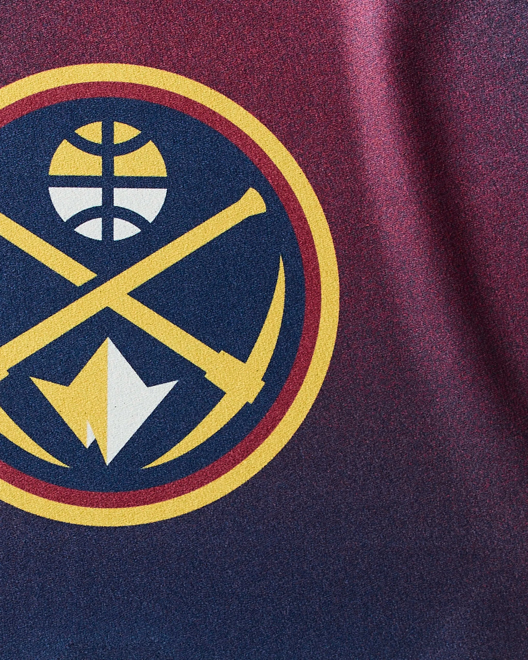 A close-up of the Nuggets Fade gym towel by Geometry, featuring the Denver Nuggets logo with crossed pickaxes and mountain in a gold circle on quick-drying blue and maroon fabric.