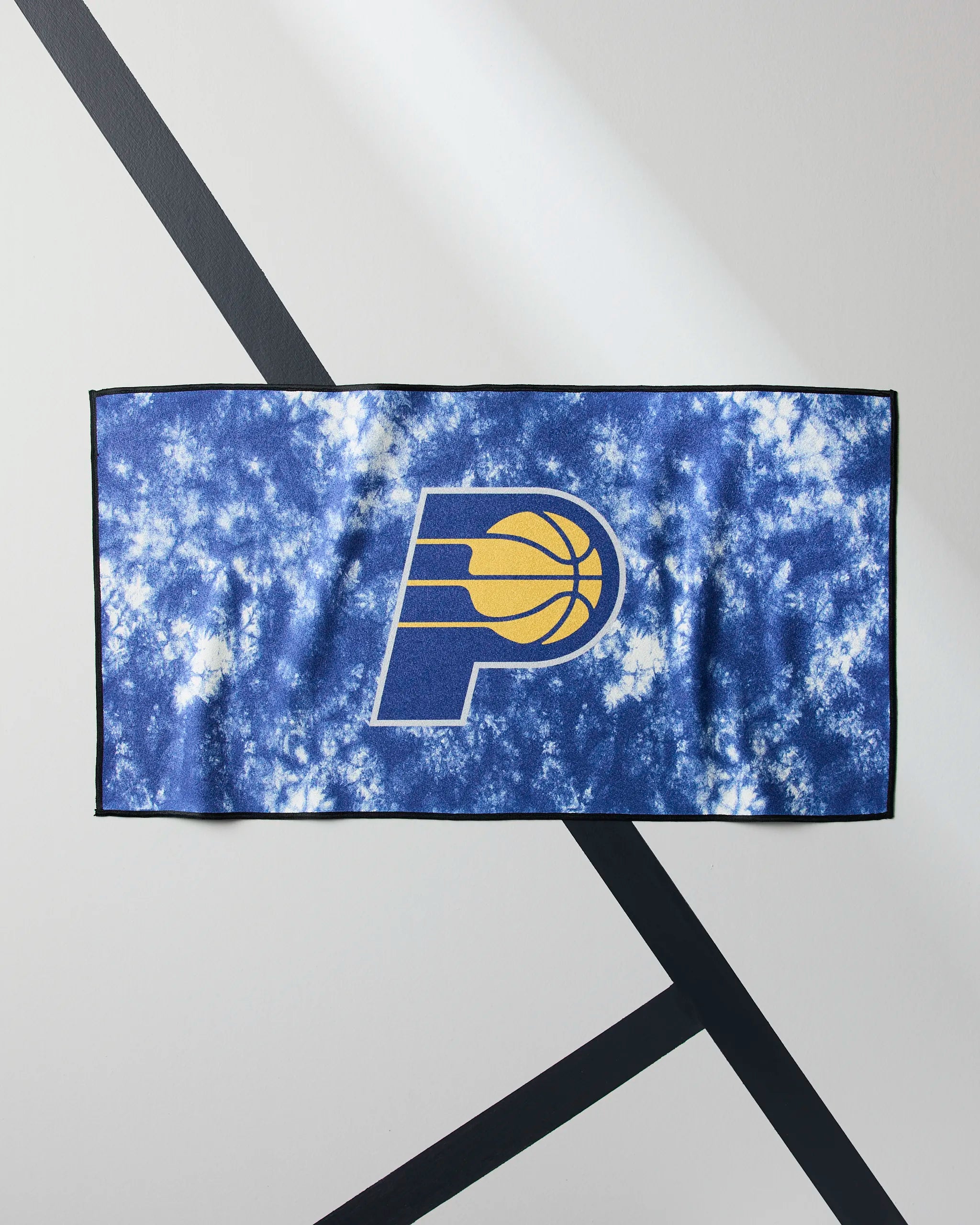 The Geometry Pacers Flash is a blue and white tie-dye NBA fitness towel featuring the Indiana Pacers logo in the center, shown on a light gray surface with diagonal black lines.