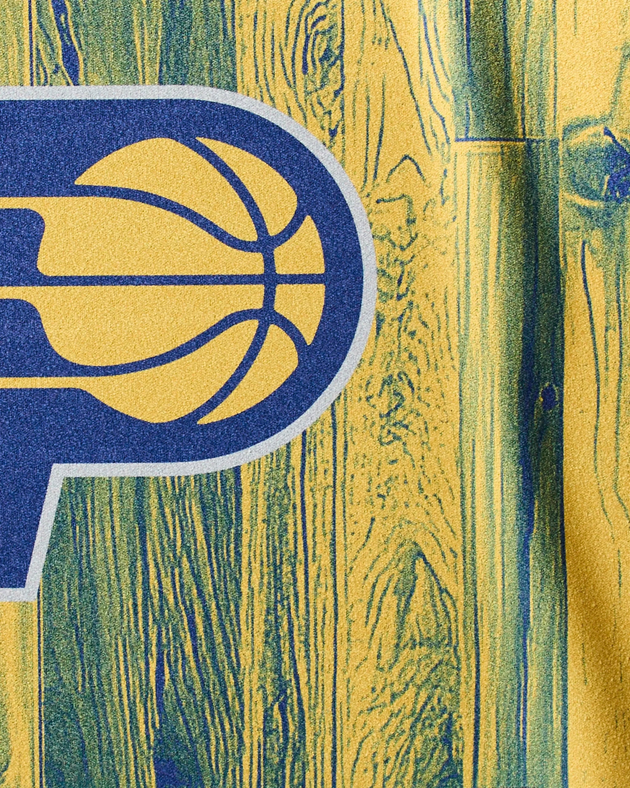 Close-up of the Indiana Pacers stylized "P" logo on a yellow and blue wood-patterned background, featured on Geometry's Pacers Zone quick-drying NBA fitness towel—designed for workouts and gym sessions.