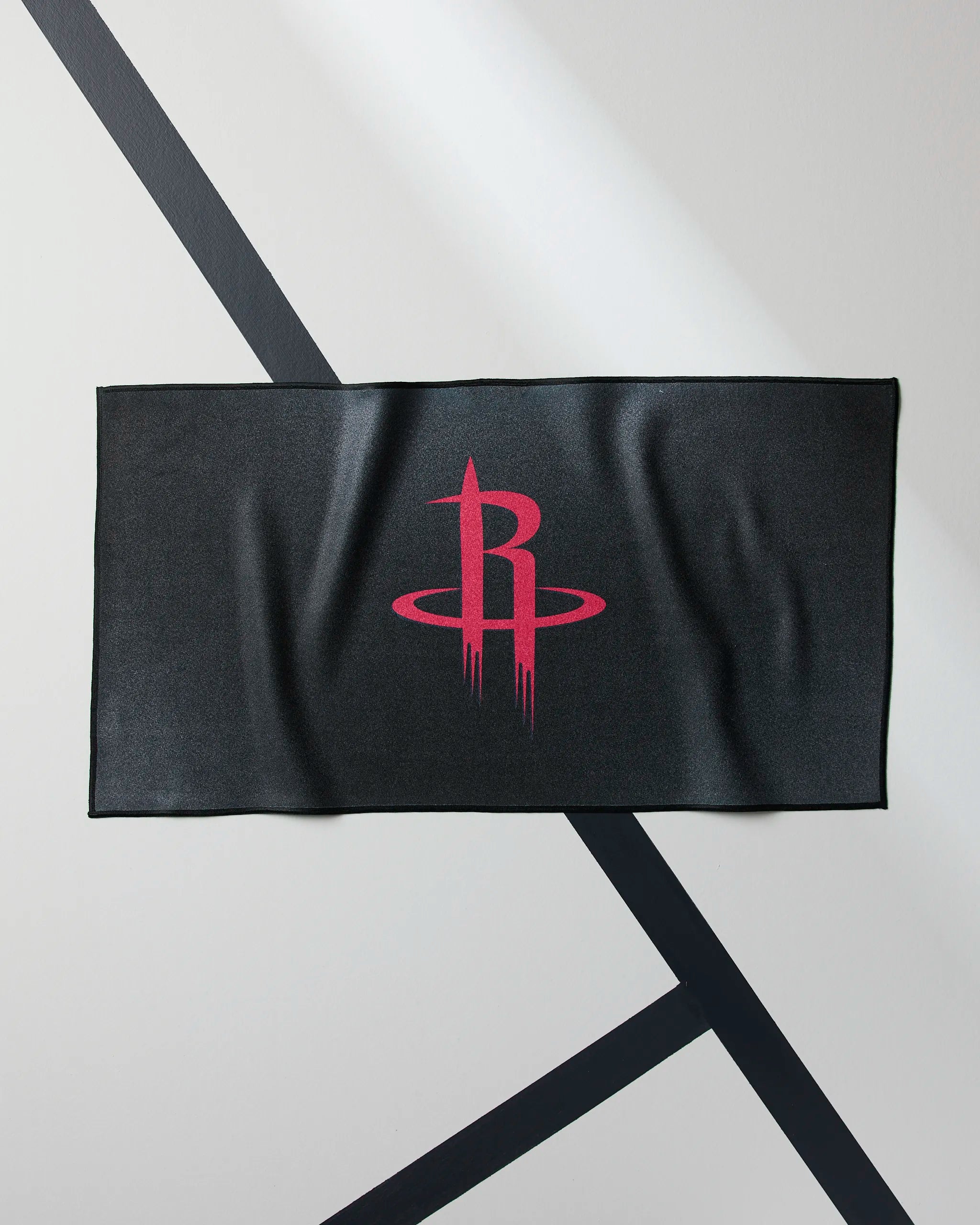 The Rockets Fade by Geometry is a black rectangular NBA fitness towel showcasing the red Houston Rockets logo, displayed flat on a white background with intersecting black lines.