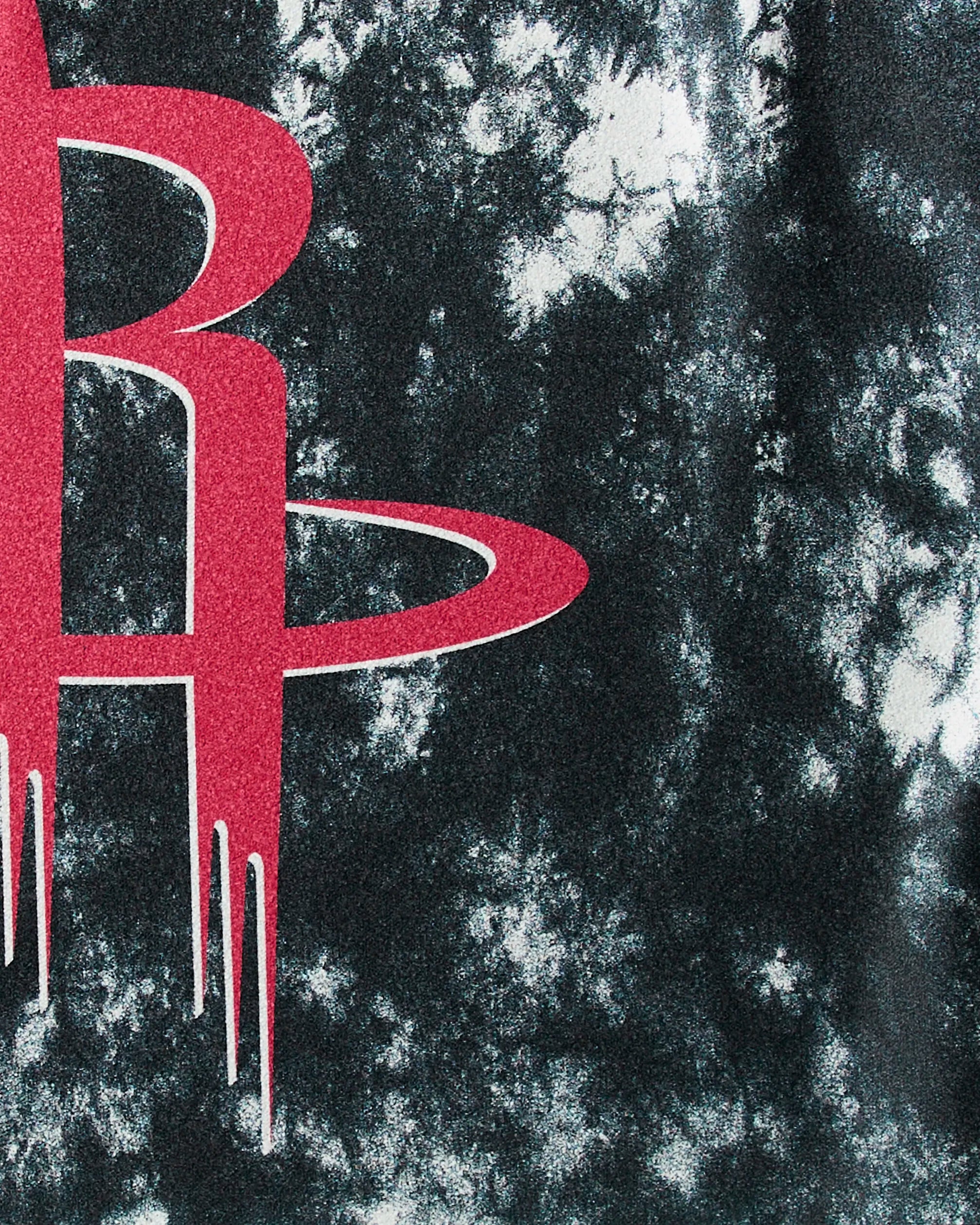 A close-up of the red Houston Rockets logo on the Rockets Flash fitness towel by Geometry, featuring a black and white tie-dye pattern. This quick-drying NBA towel is ideal for eco-conscious fans and active workouts.