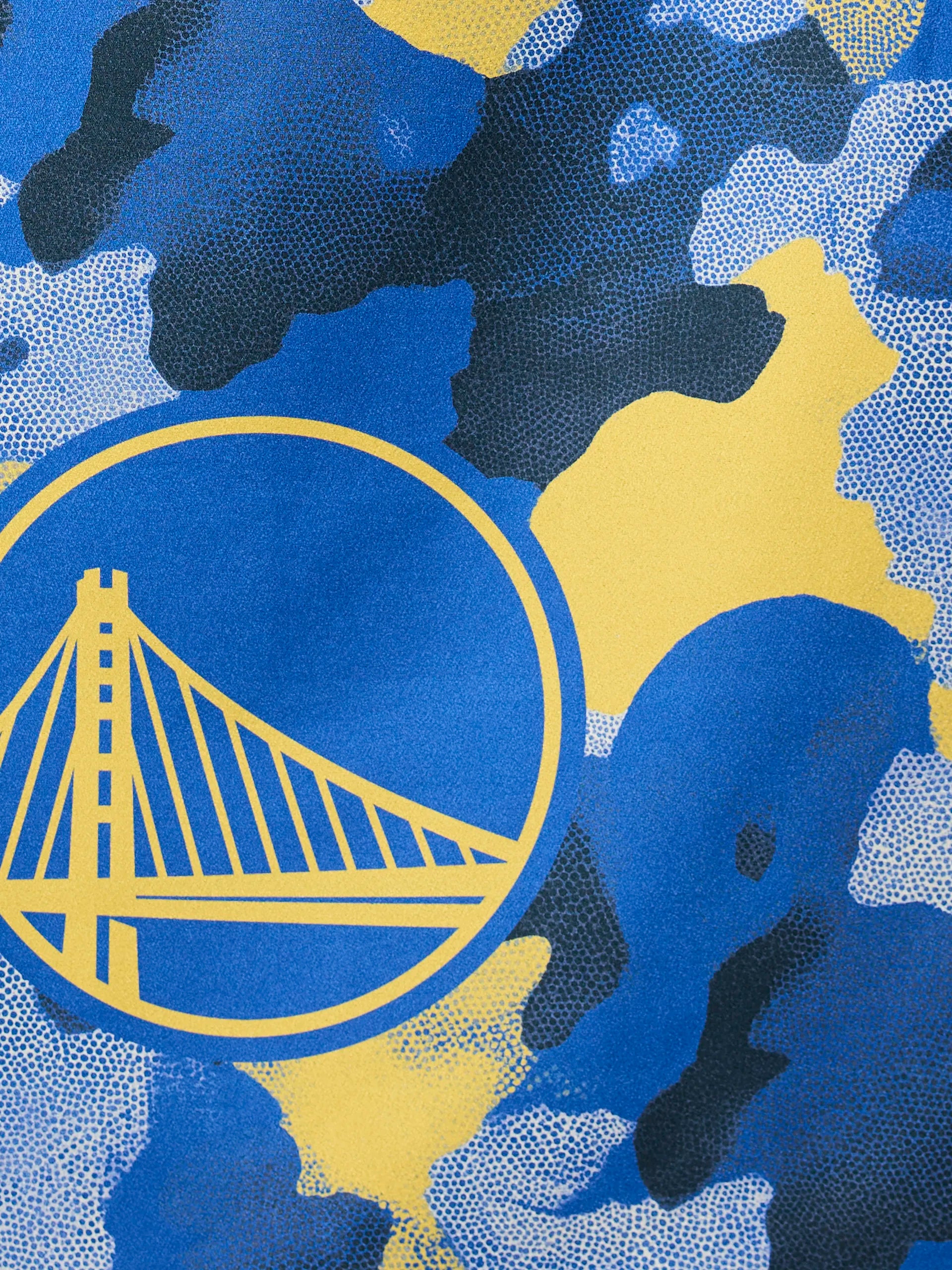 The Warriors Camo by Geometry features a stylized yellow Golden Gate Bridge inside a circle, set on a blue, yellow, and black camouflage-patterned background.