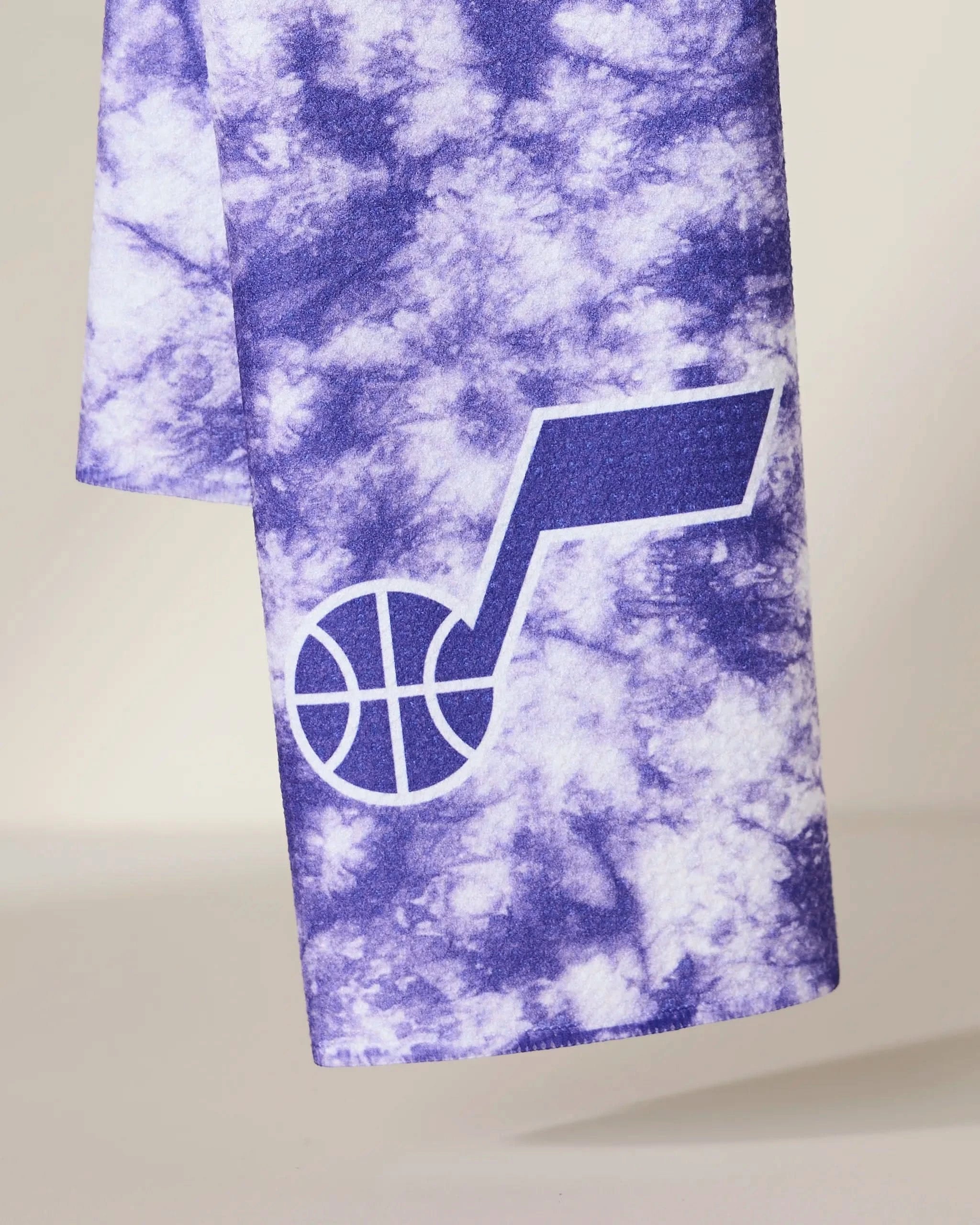 The Geometry Jazz Flash towel features a purple and white tie-dye design with the Utah Jazz team logo in white on the lower section.