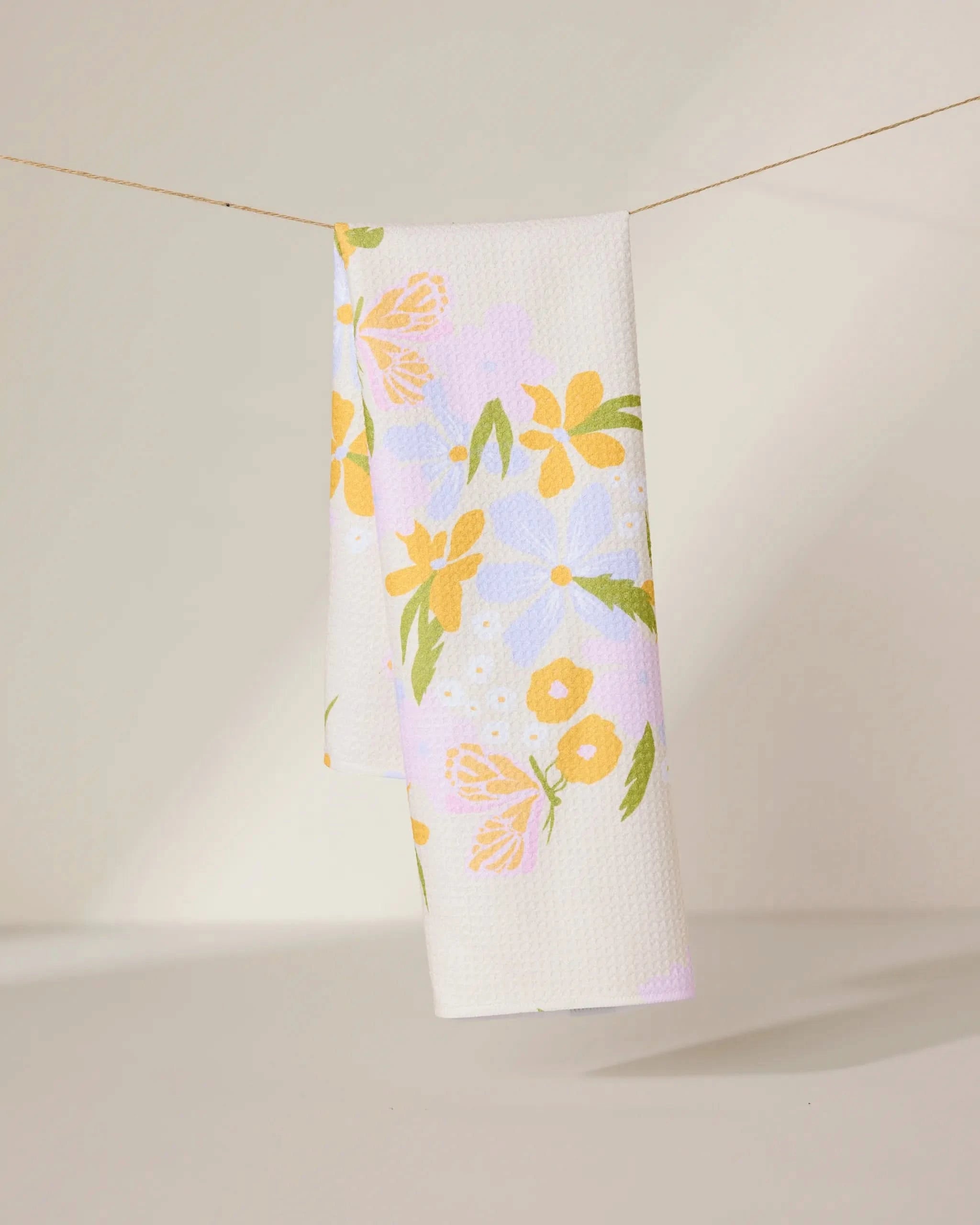 The GEOMETRY Abloom tea towel, made from ultra-absorbent recycled materials, features a white background with yellow, orange, and purple flowers and green leaves—perfect for brightening any kitchen.