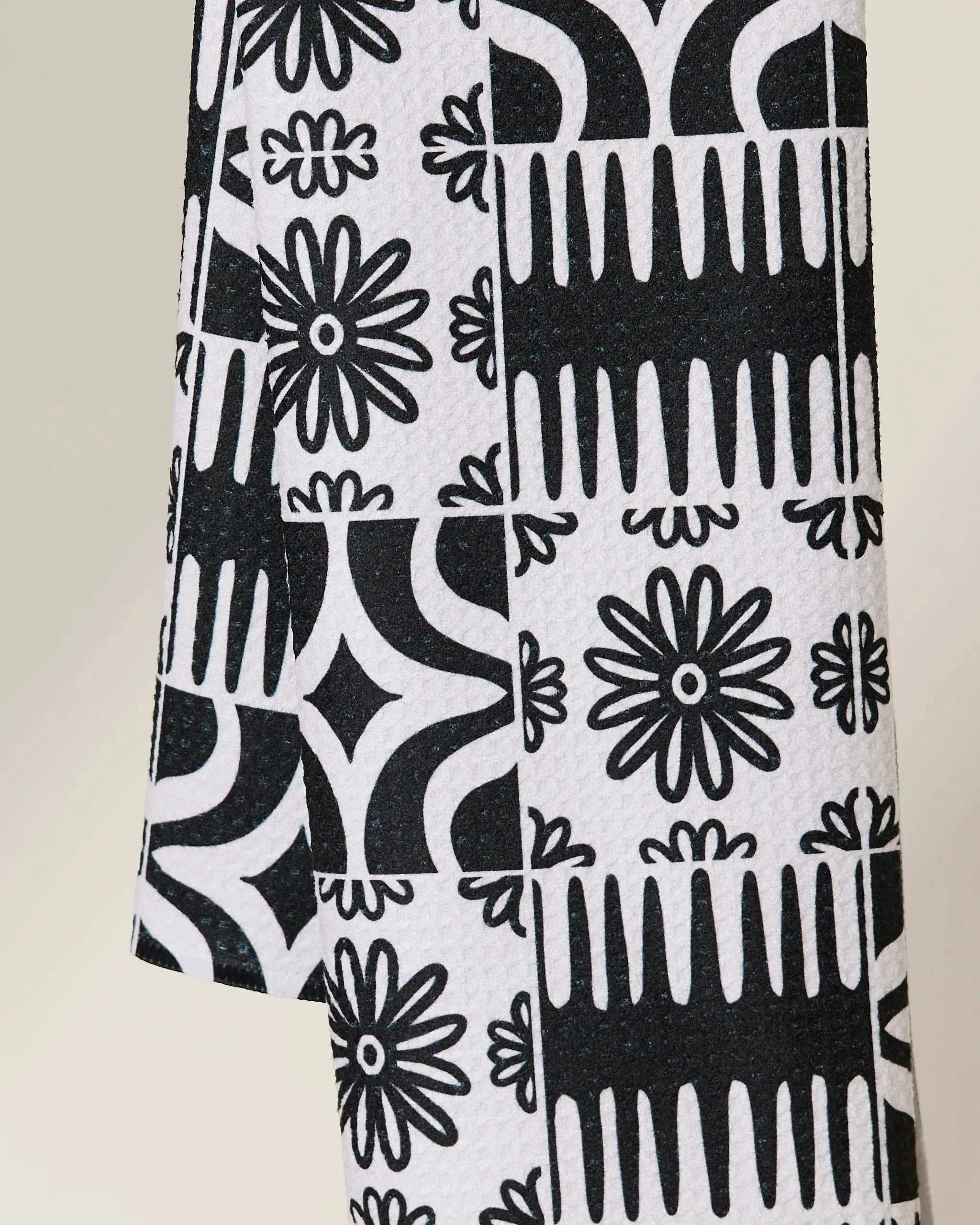 The GEOMETRY Bohemian Mosaic is a quick-drying towel showcasing black and white geometric and floral motifs—daisies, diamonds, and abstract shapes—in a repeating grid design.