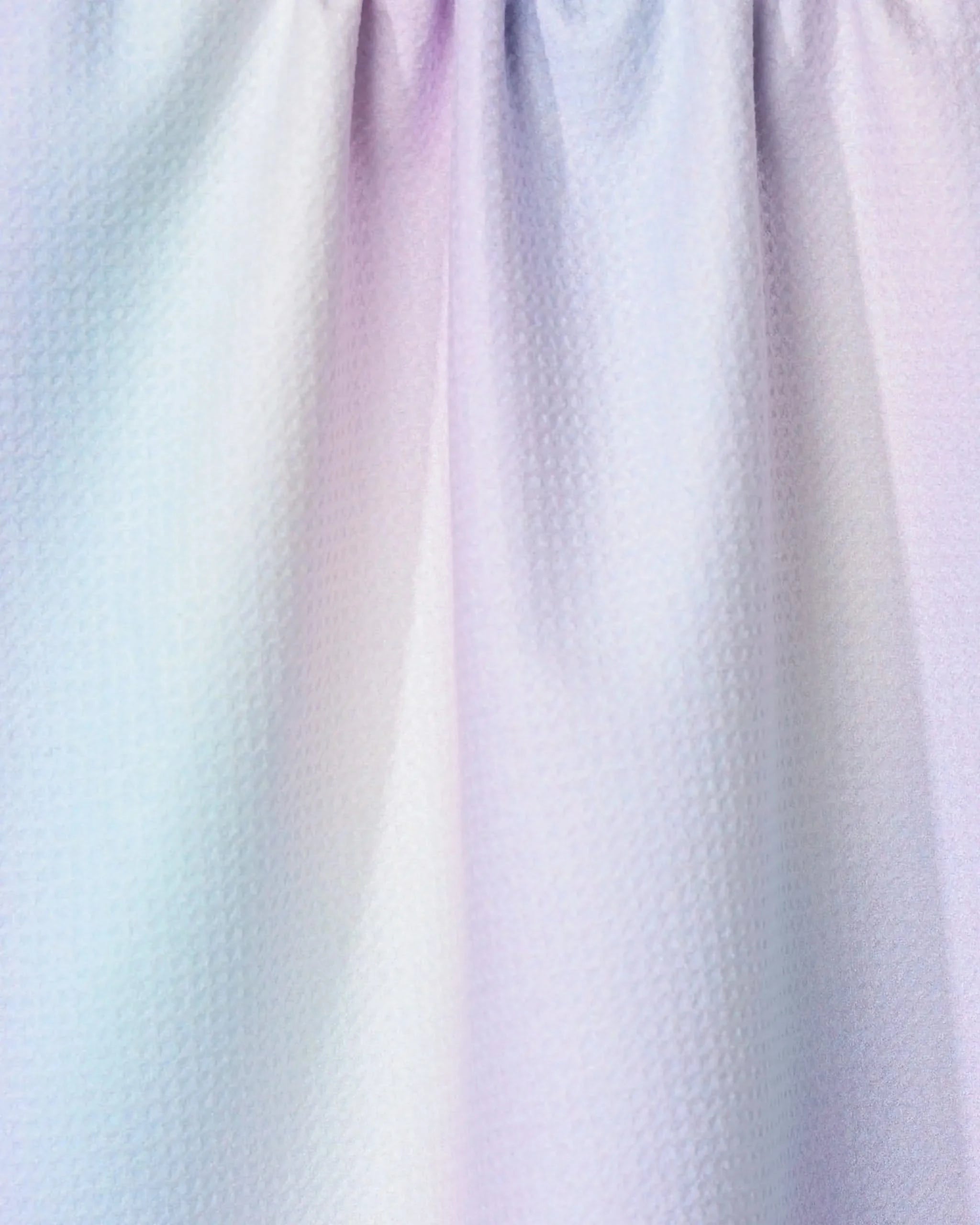 Close-up of the GEOMETRY Iridescence tea towel, featuring pastel hues of light blue, pink, and purple with a textured finish. The ultra-absorbent kitchen towel has soft folds and is gently gathered at the top.