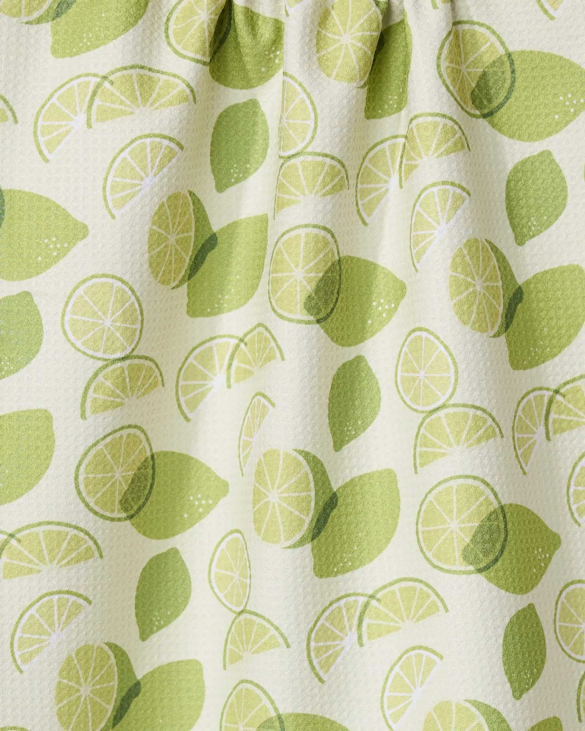 A close-up of the GEOMETRY Limes recycled kitchen towel, showing whole and sliced lime patterns in green on a light background. The fabric is slightly textured and gathered at the top.