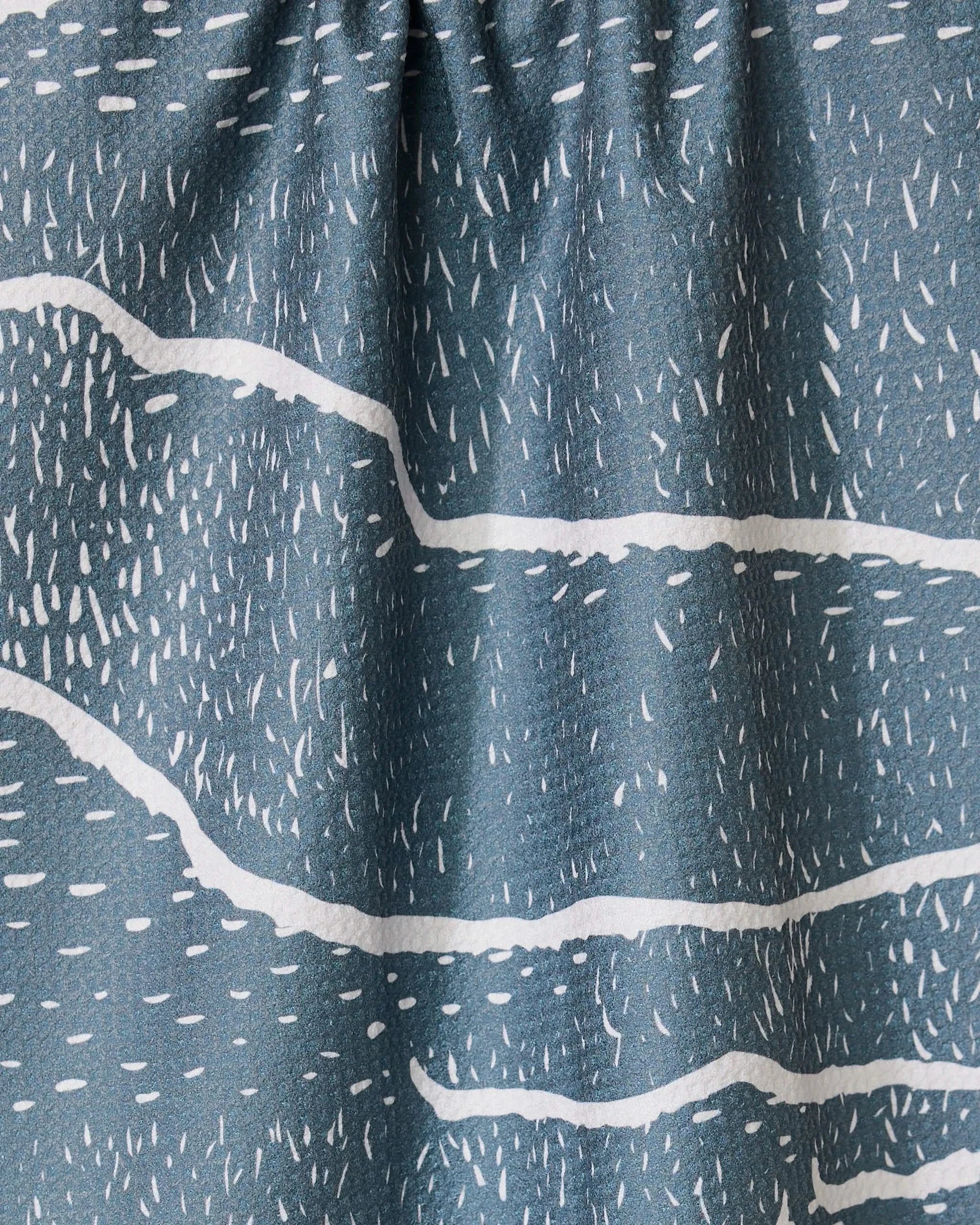 Close-up of GEOMETRY’s Wetlands - Midnight dish towel, featuring a blue-gray absorbent fabric with white abstract wavy lines and dash patterns for a textured, artistic look.