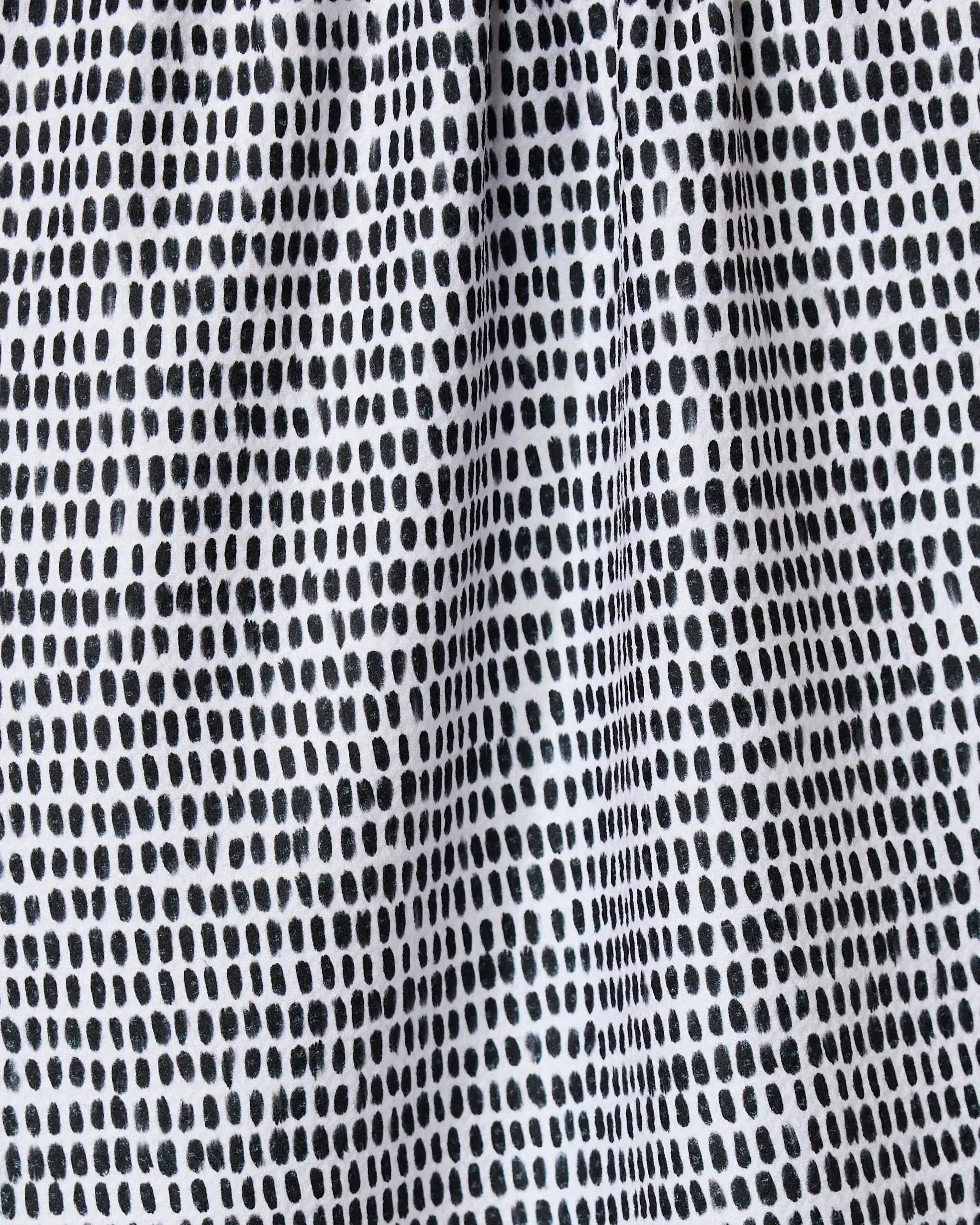 Close-up of Geometry’s Dot Dot Dot Fresh Linen kitchen towel, featuring a grid-like pattern of irregular black dots on white recycled fabric with a lightly gathered, textured look.