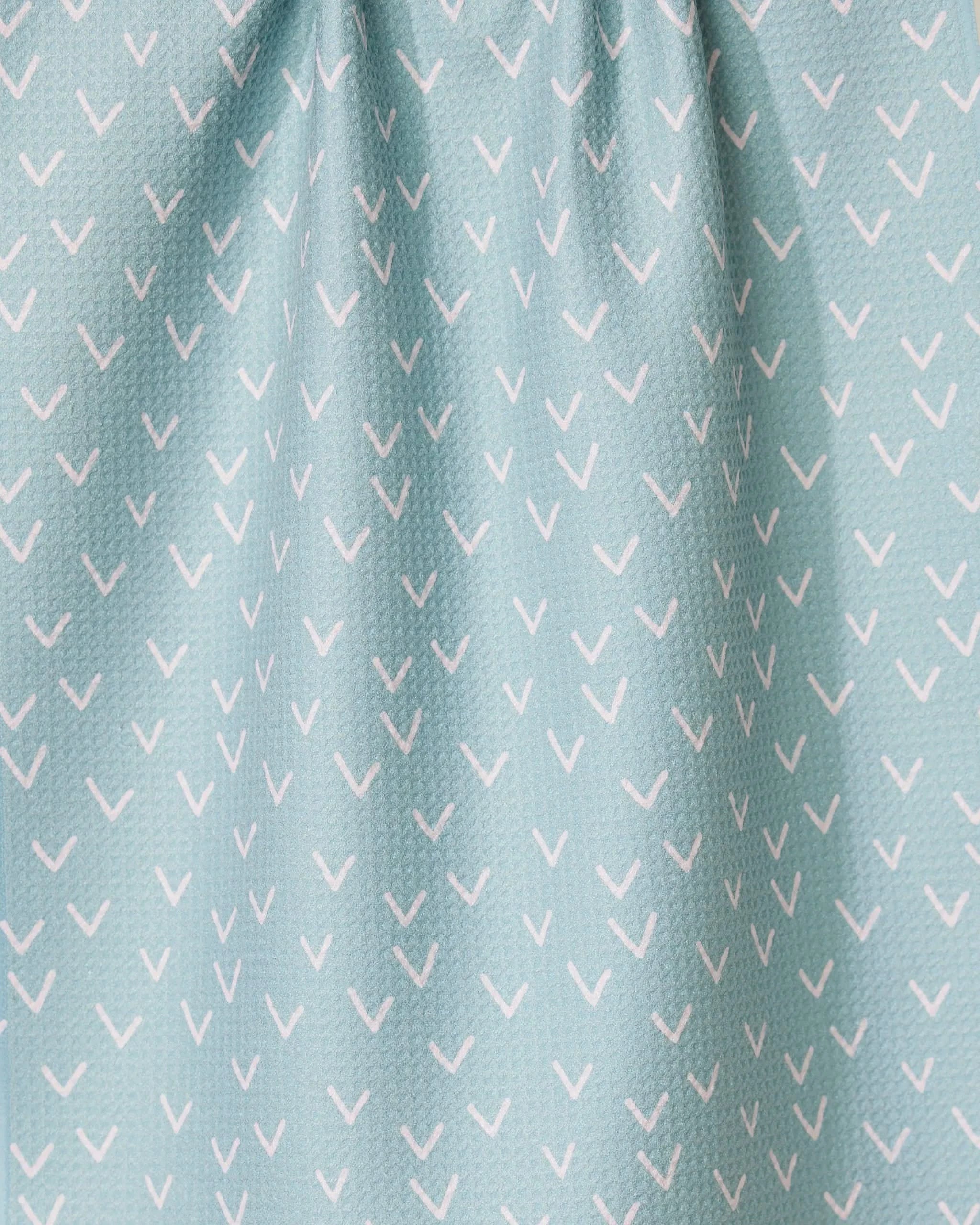 The Drawn Doves tea towel by GEOMETRY features a light blue color with small white check marks in diagonal rows, made from quick-drying fabric and gently gathered at the top.