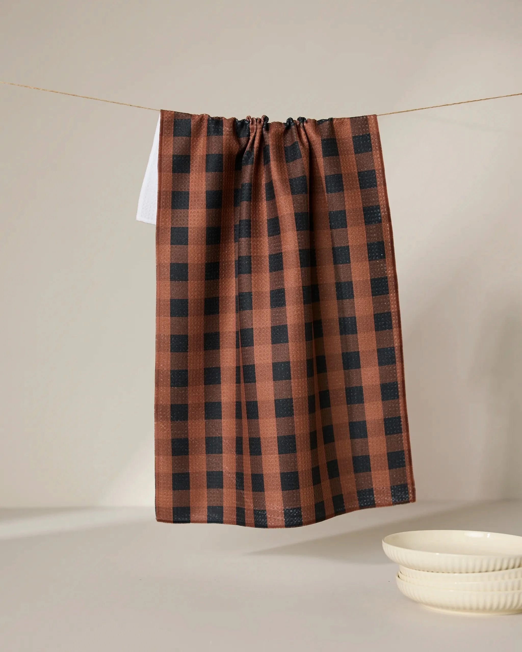 The GEOMETRY Fall Gingham tea towel hangs from a string against a plain light background, with two stacked cream-colored bowls placed nearby.