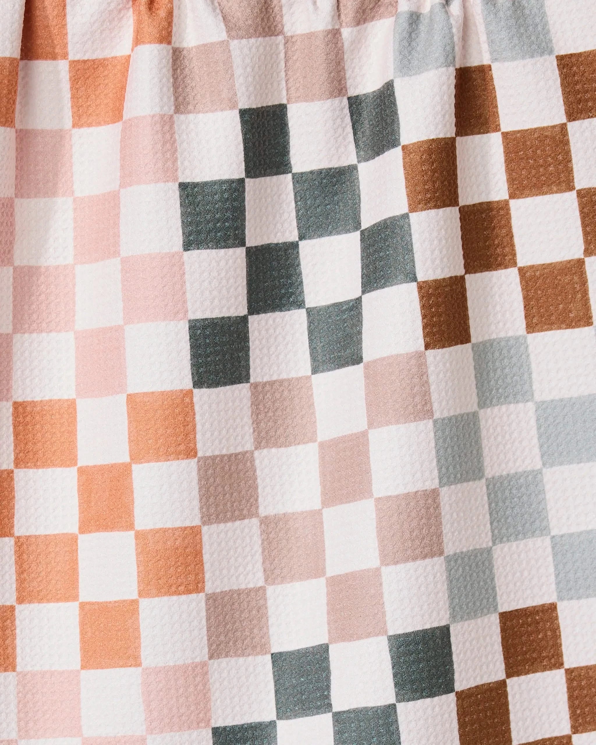 A close-up of the GEOMETRY Autumn Checkers towel shows its ultra-absorbent, crinkled fabric with a checkered pattern in muted pink, brown, gray, and white. Even lighting highlights the unique texture and evenly spaced squares.