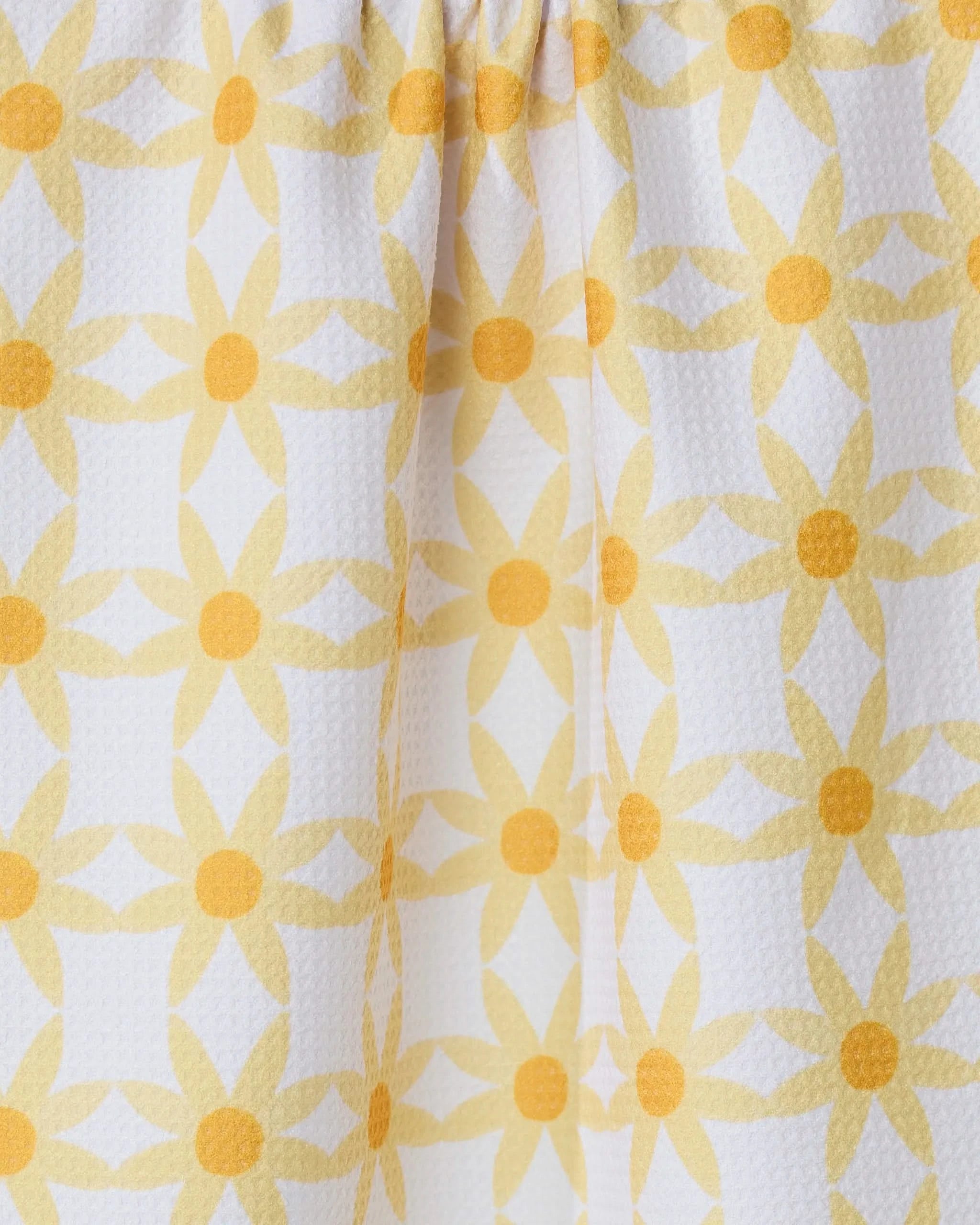 Close-up of the GEOMETRY Daisies kitchen tea towel, featuring a repeating yellow floral pattern with circular centers on white, ultra-absorbent textured fabric and gentle folds.