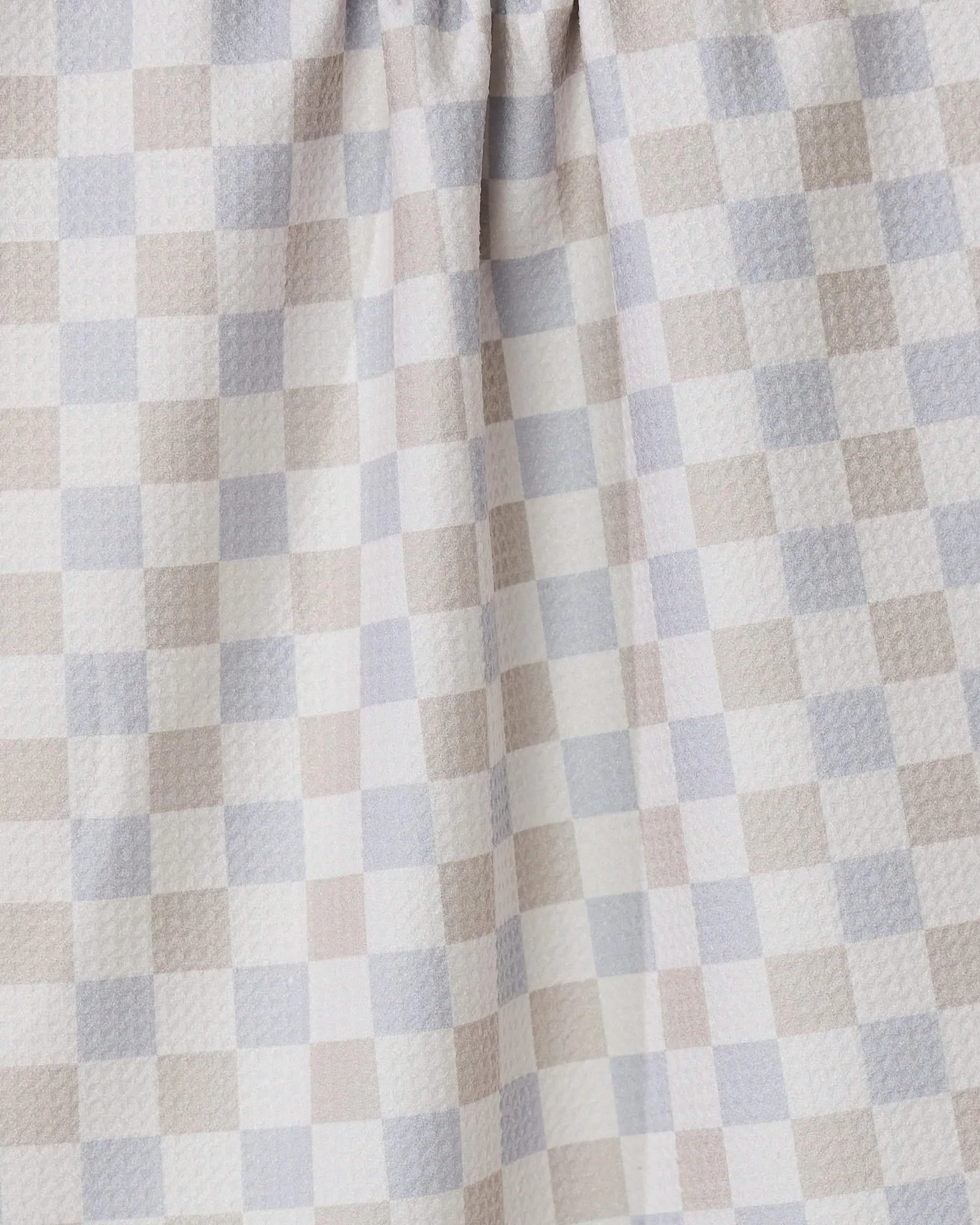 A close-up of the Danse Neutre quick-drying towel by GEOMETRY, featuring a checkered pattern in soft beige, light gray, and white. The fabric is gently gathered at the top, highlighting its texture and folds.