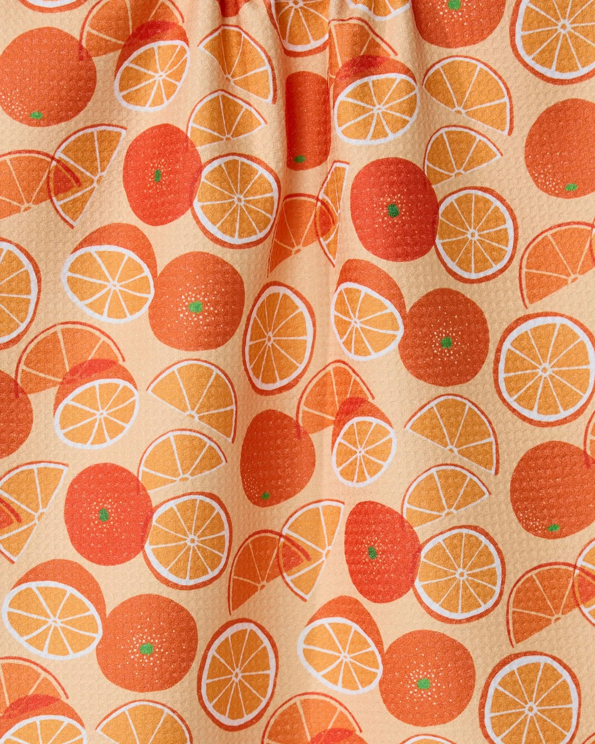 The Geometry Only Oranges tea towel features whole and sliced oranges in orange and yellow hues on a light peach background.