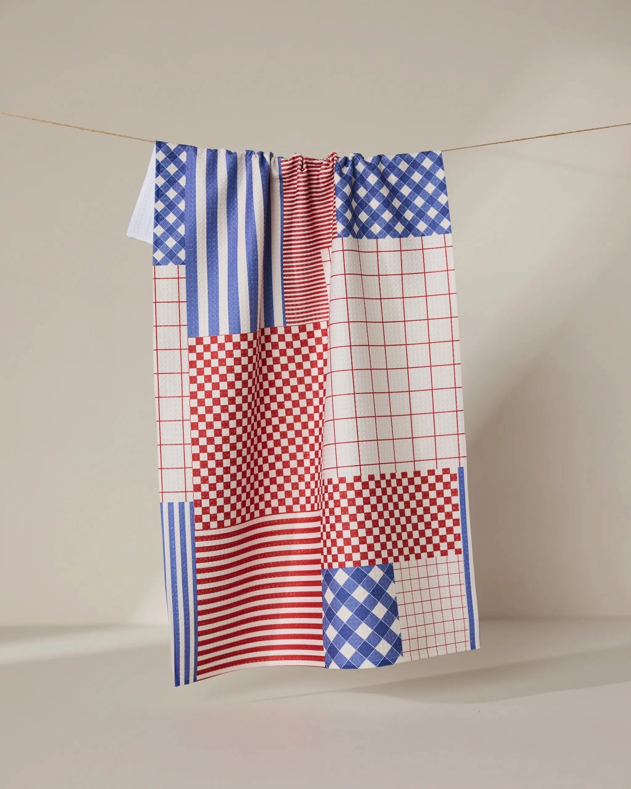 The Geometry Patched Up Parade ultra-absorbent dish towel hangs neatly on a rope.