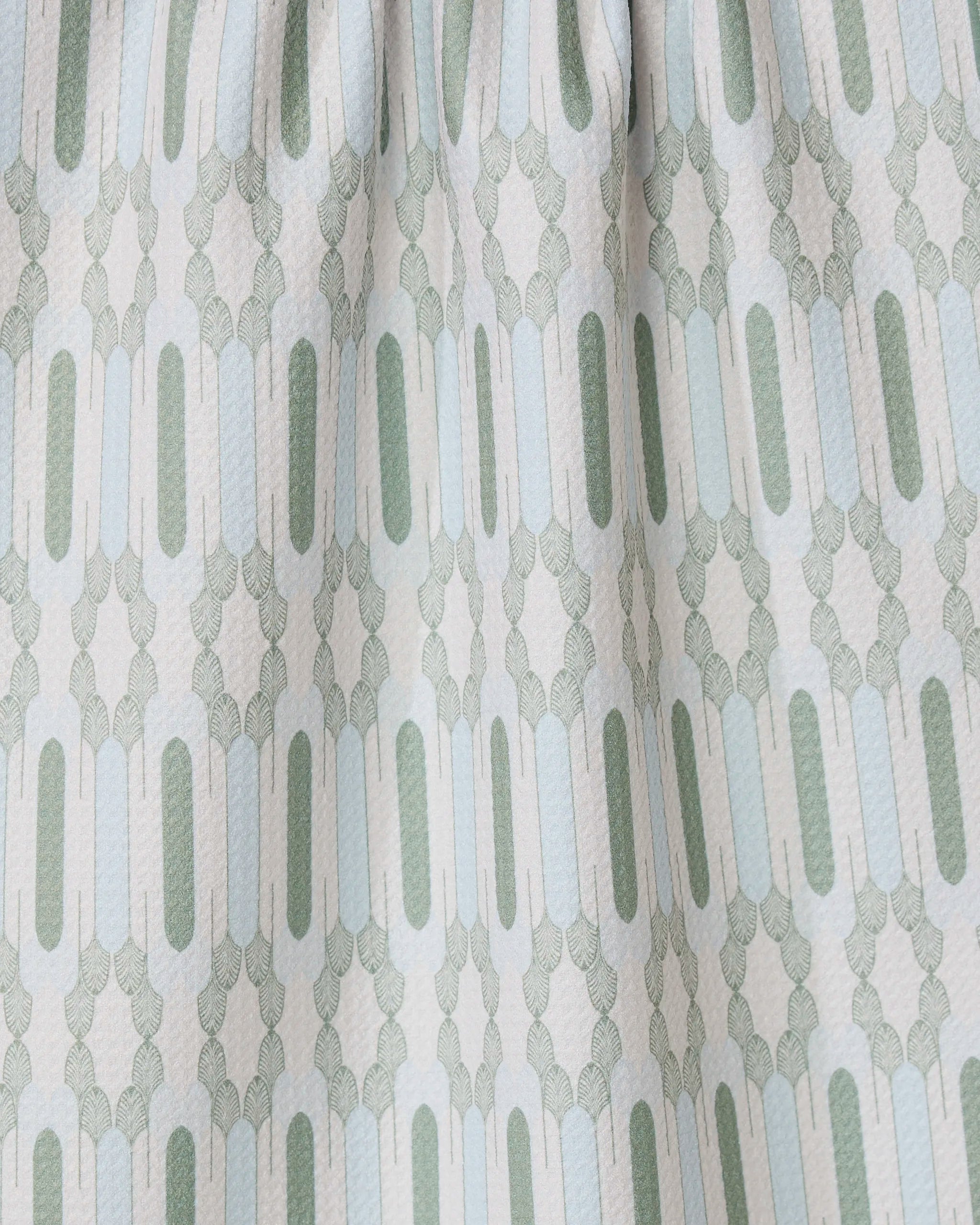 Close-up of the Musée Verte tea towel by GEOMETRY, showcasing a repeating geometric pattern in light green and gray. Made from recycled materials, it features elongated ovals and small shapes with gently gathered fabric at the top.