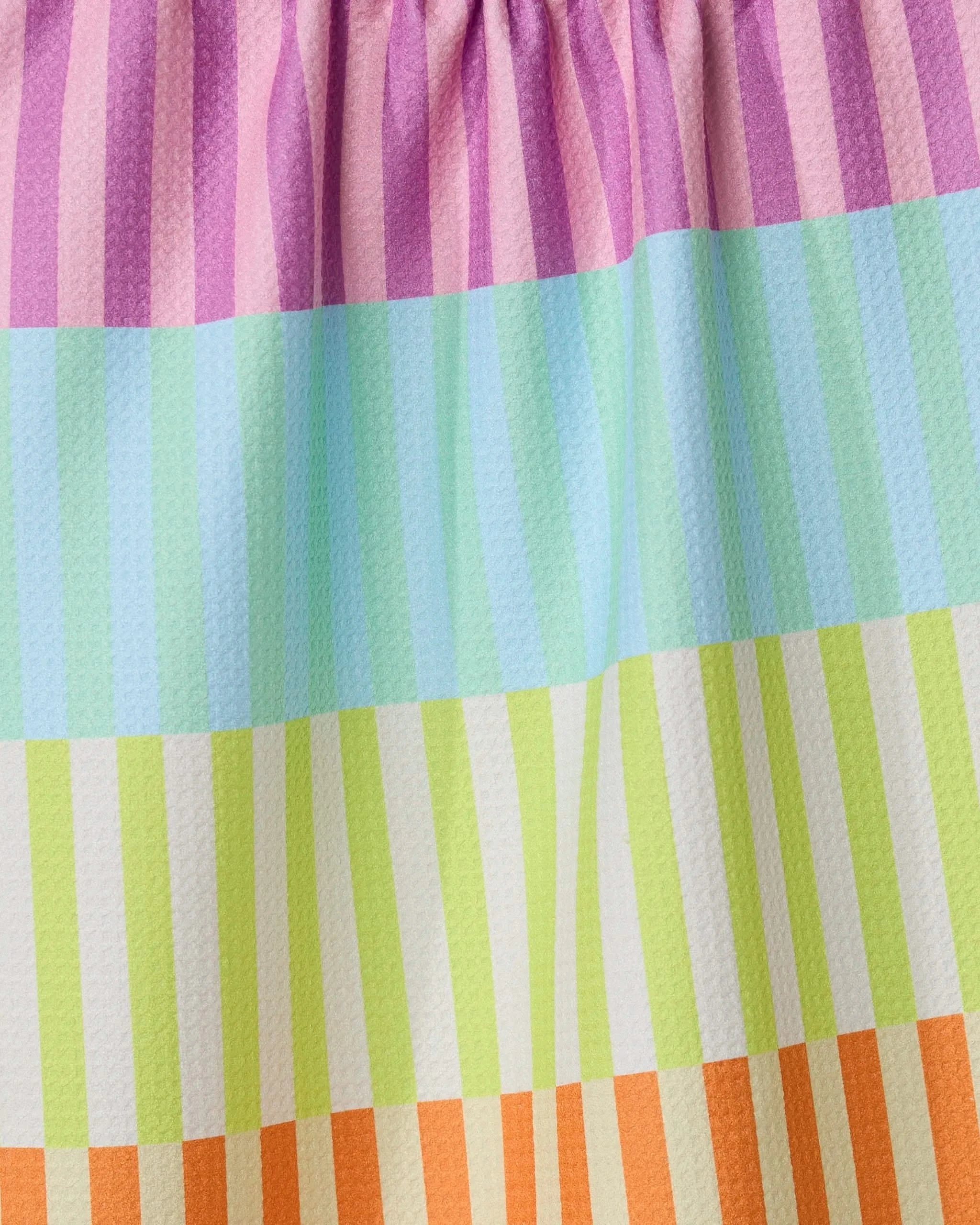 Close-up of the GEOMETRY Neon Nights towel, a quick-drying design with horizontal pastel stripes in pink, purple, blue, green, yellow, and orange. The gathered fabric at the top creates gentle folds and soft shadows.