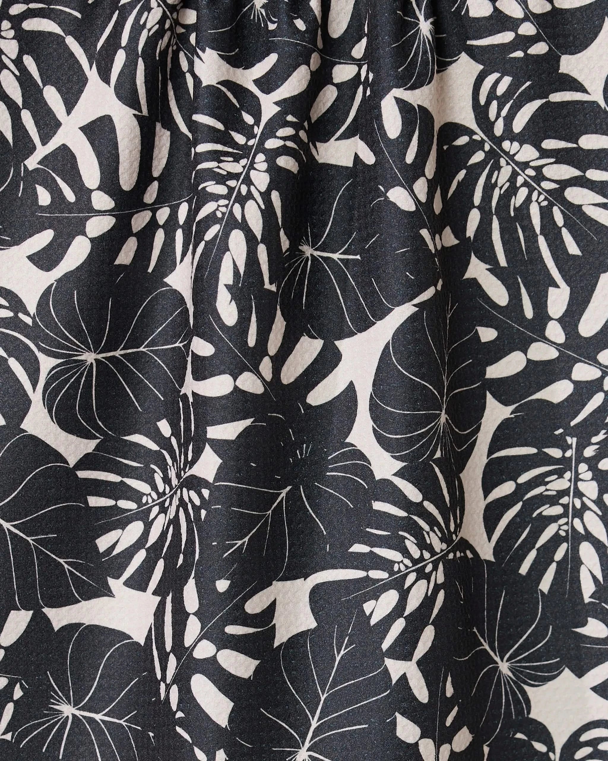 Close-up of GEOMETRYs Neutral Leaves tea towel, made from ultra-absorbent fabric with a black and white stylized monstera leaf pattern on a light background. Fabric is slightly gathered at the top.