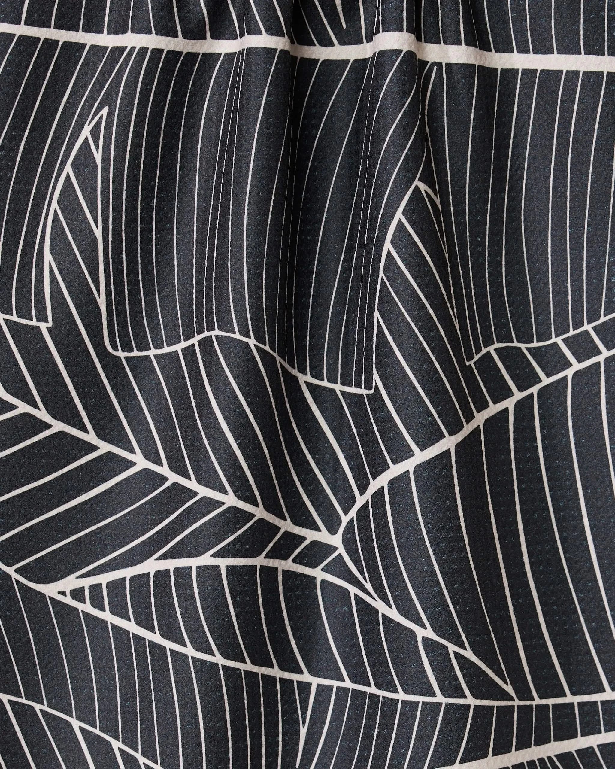 Close-up of GEOMETRYs Neutral Palms: black fabric with bold white geometric palm patterns. The gathered top forms soft pleats and shadows, creating an elegant, modern look.