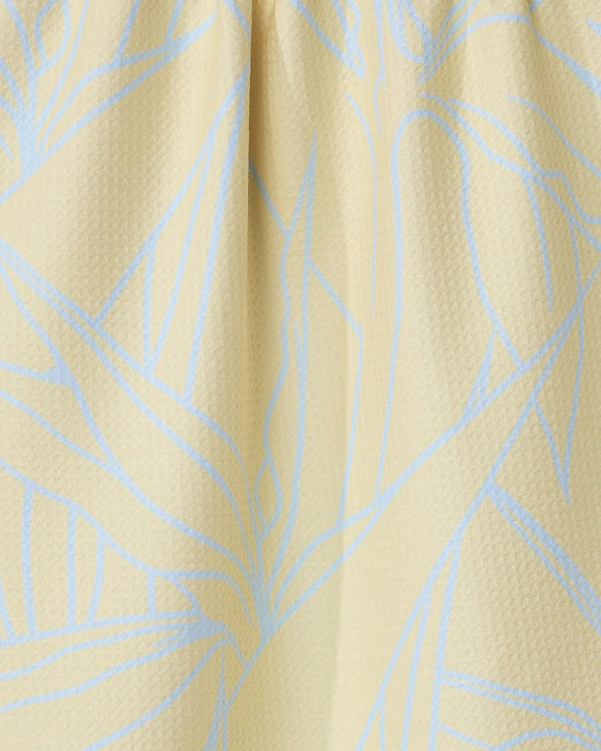Close-up of the Paradise Blooms tea towel by GEOMETRY, featuring a textured light yellow fabric with a subtle blue abstract leaf pattern and soft folds near the top.