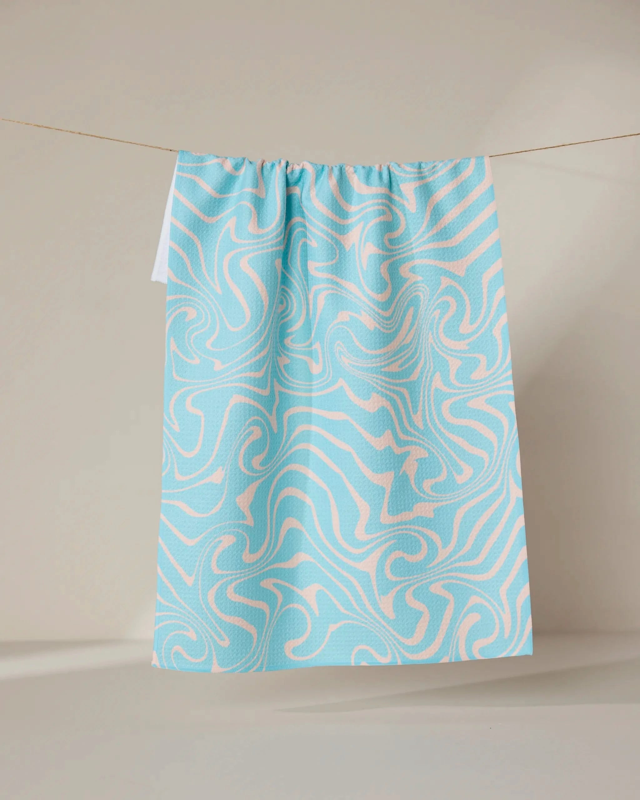 The GEOMETRY Patience tea towel, featuring a blue and white abstract swirl design, hangs against a neutral backdrop. Made from recycled materials, it’s both eco-friendly and quick-drying.