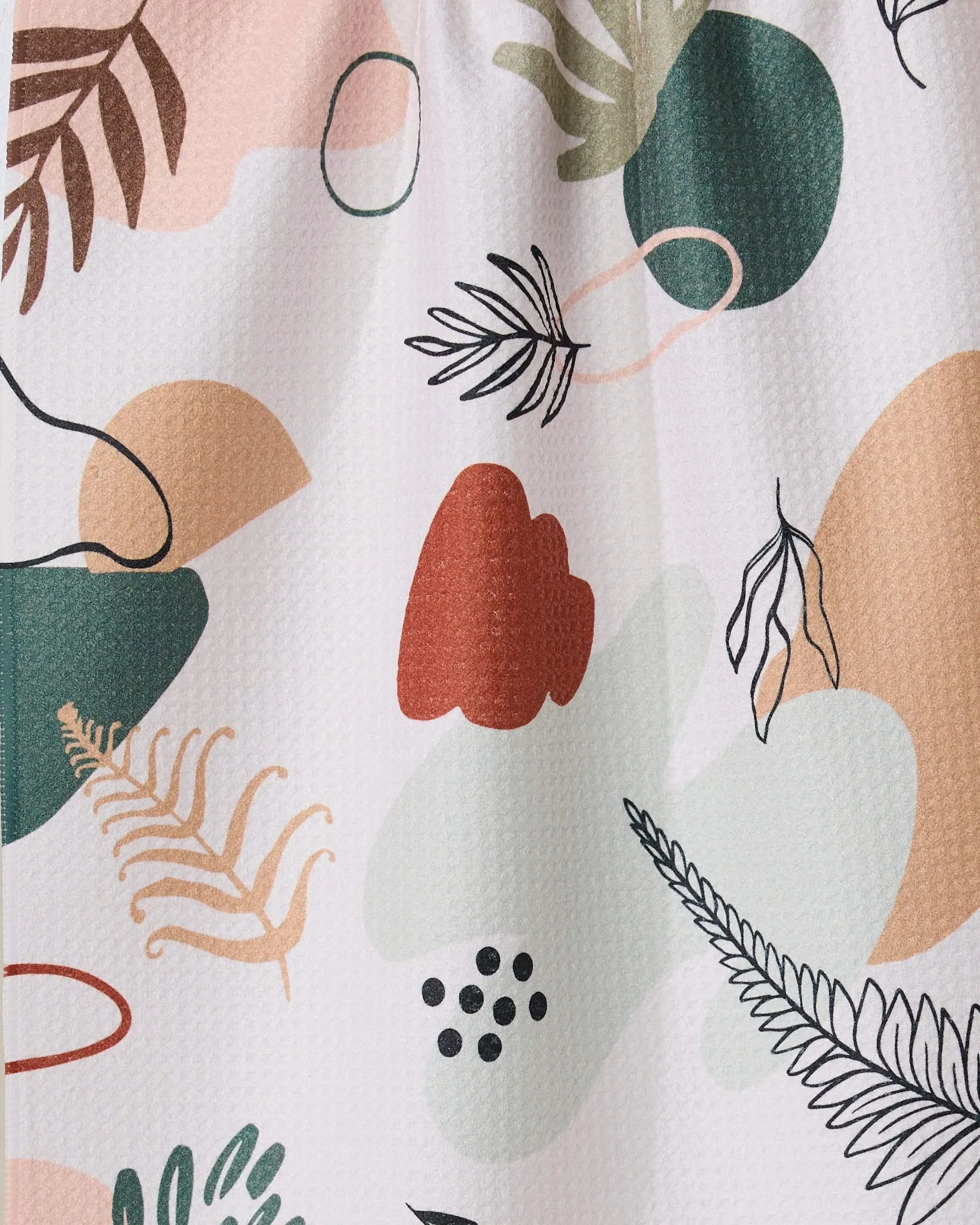 Plated Ferns by GEOMETRY features an abstract pattern of organic shapes and botanical elements in green, peach, black, and red on a light background. This playful, modern tea towel is made from recycled materials.