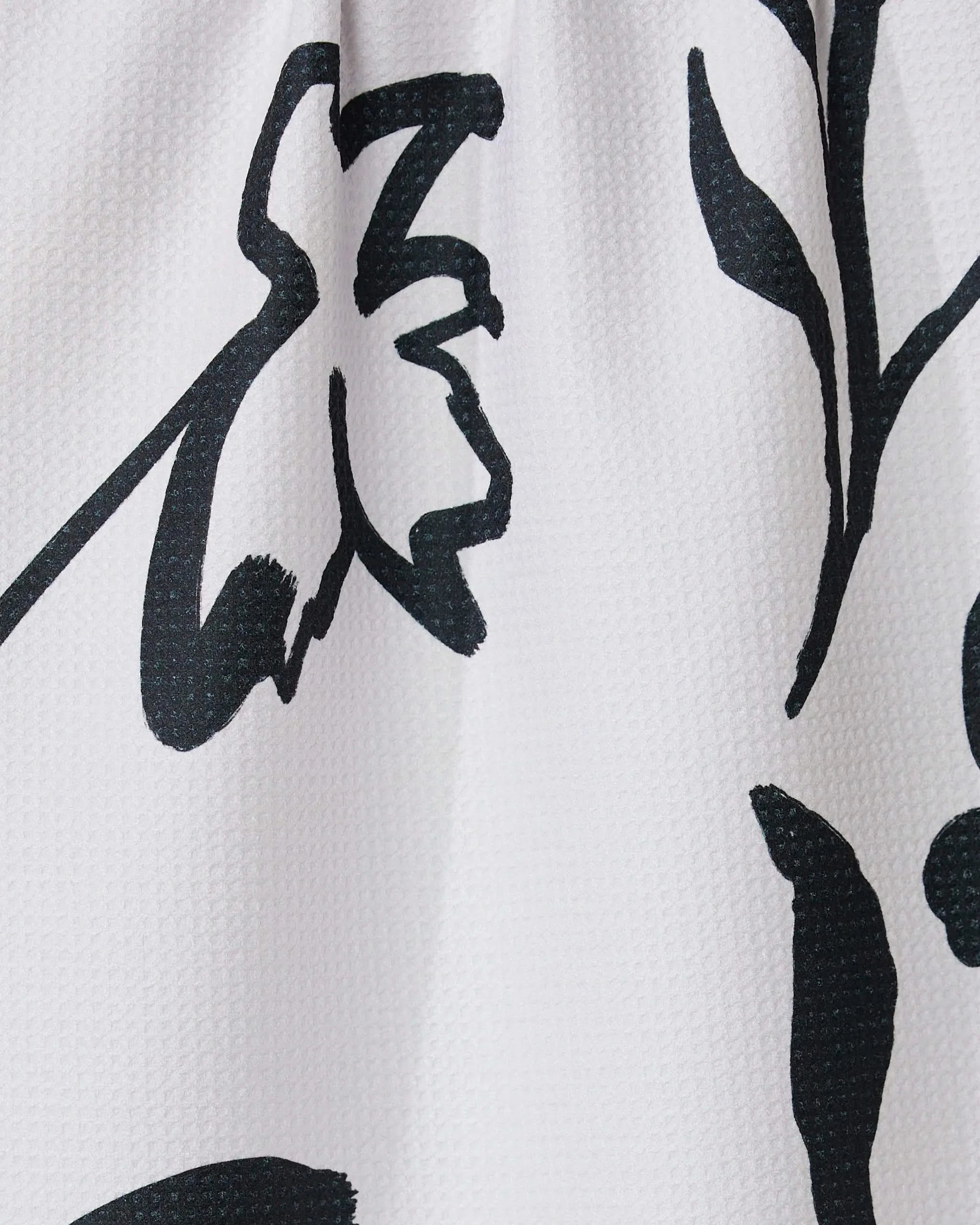 Close-up of the Shade tea towel by GEOMETRY, crafted from recycled materials. It features a bold black abstract floral print with thick, sweeping lines forming flower and leaf shapes on a white textured background.