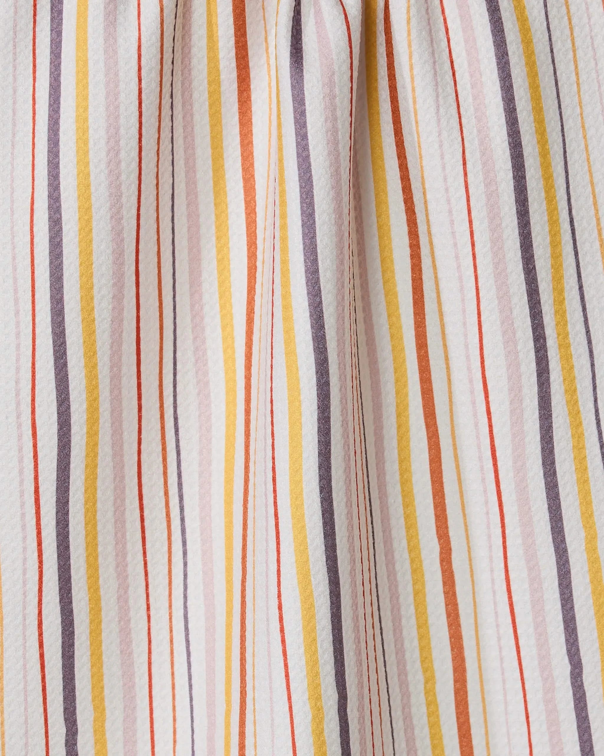 A close-up of GEOMETRY’s Stripe Season towel shows ultra-absorbent fabric with vertical yellow, orange, lavender, and red stripes on white. The towel is gently gathered, creating soft folds and shadows.