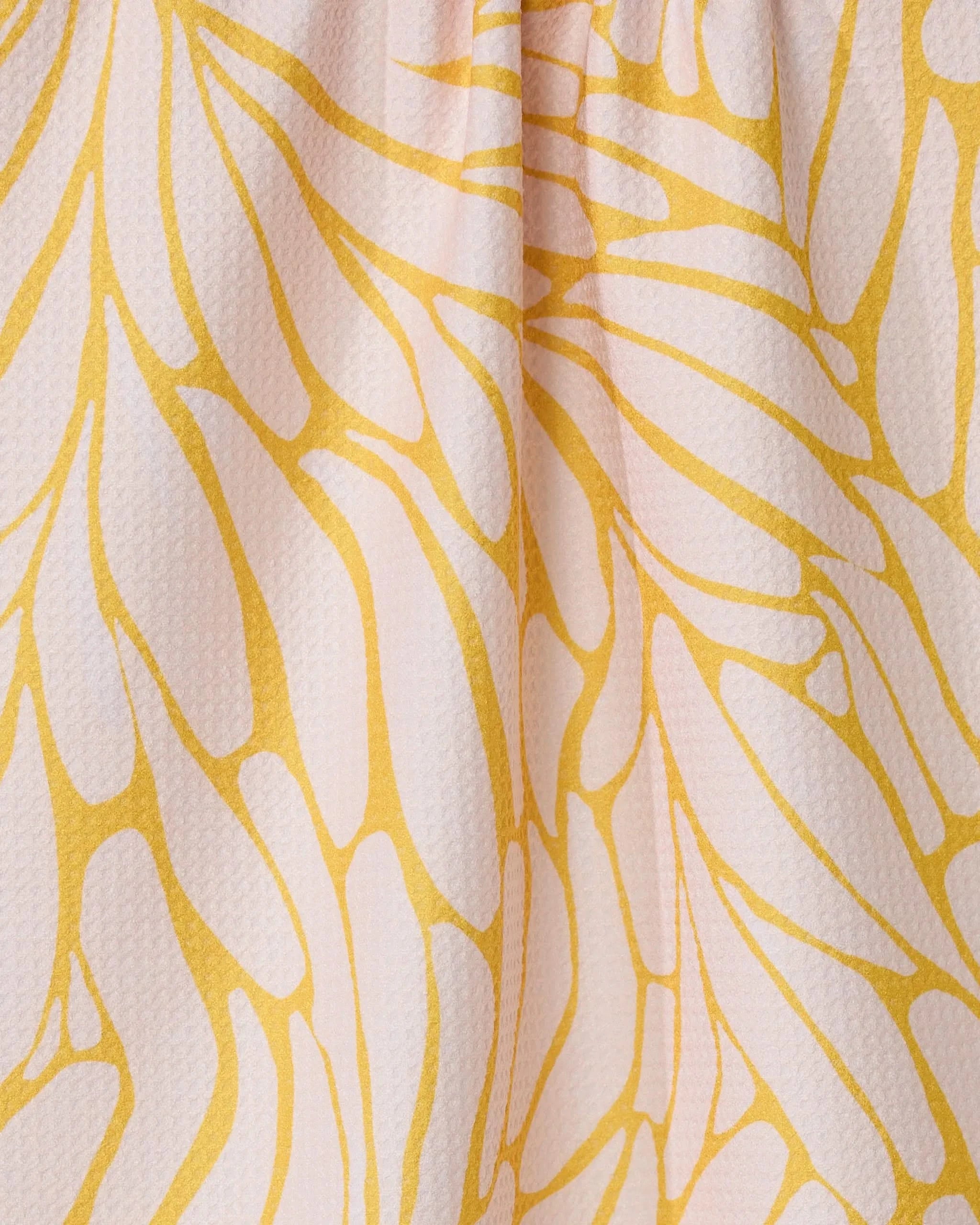Close-up of GEOMETRY’s Tenderhearted: a quick-drying tea towel made from recycled materials, featuring a textured surface and an abstract yellow-and-white leaf pattern, softly gathered for added depth.