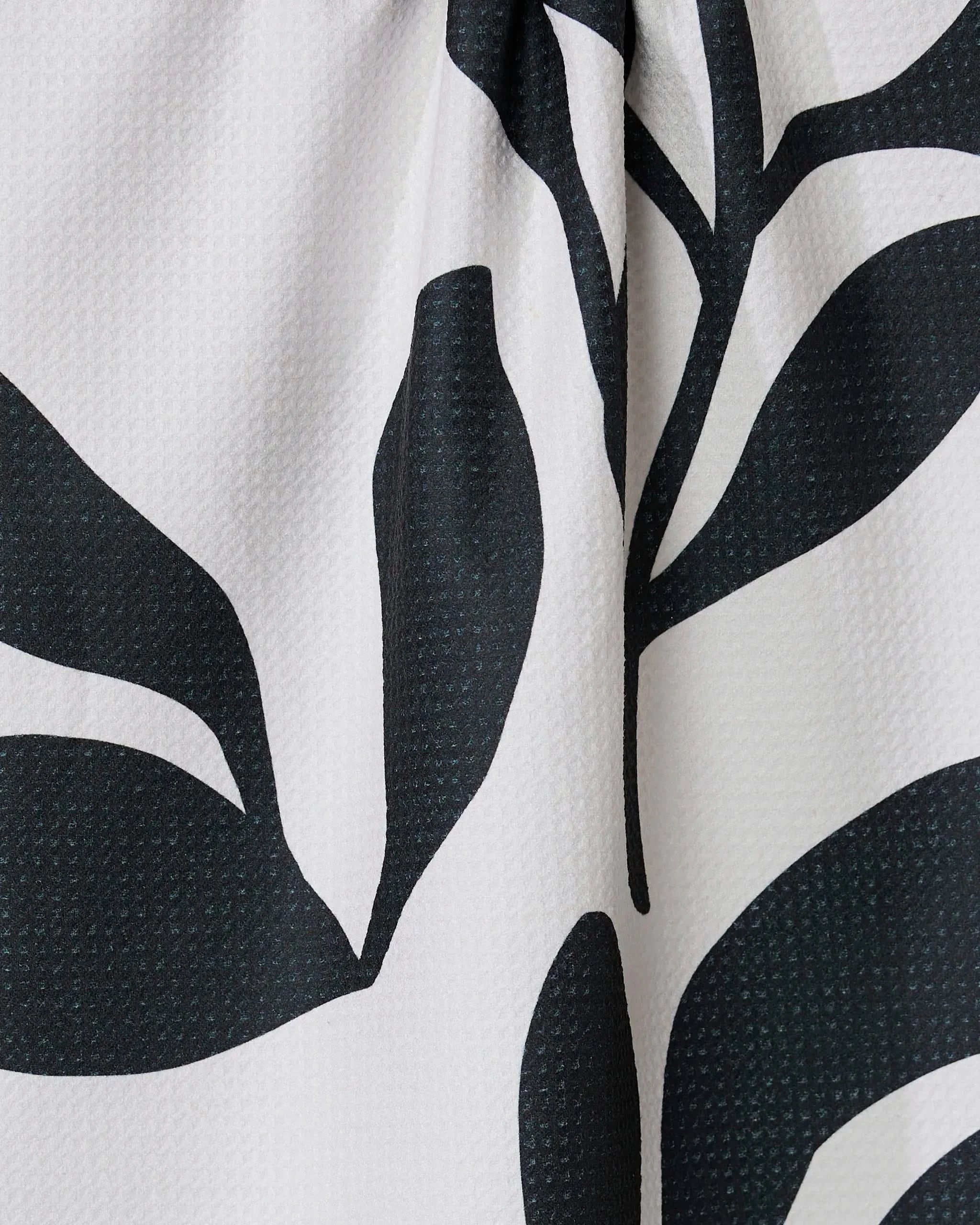 Close-up of the Threes tea towel by GEOMETRY, ultra-absorbent and made from recycled materials, featuring a bold black and white abstract leaf pattern on a textured light background.