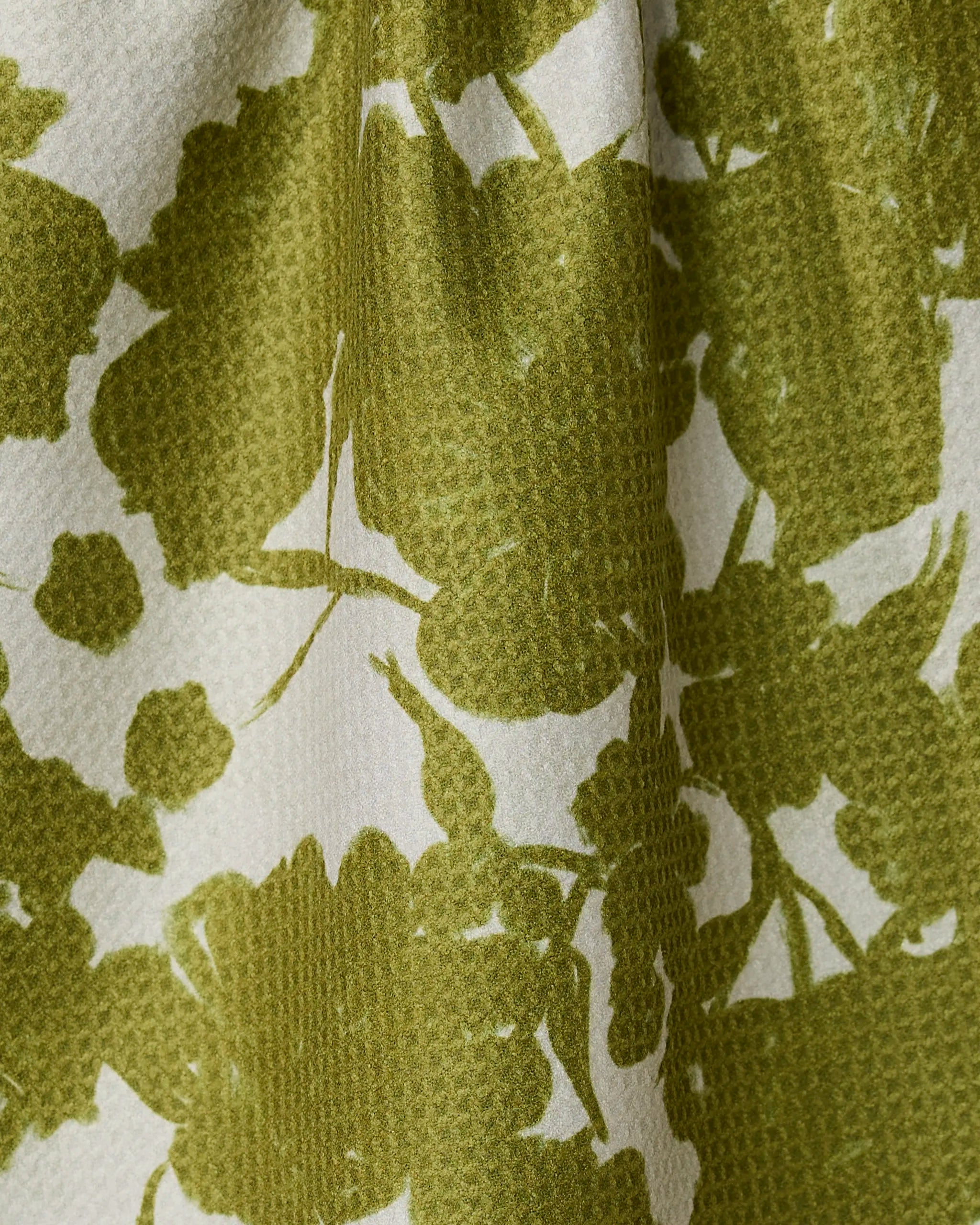 Close-up of Sweet Green by Geometry—a textured, absorbent, quick-drying kitchen towel with an olive green floral pattern on white. Soft folds and woven details add both style and function to your space.