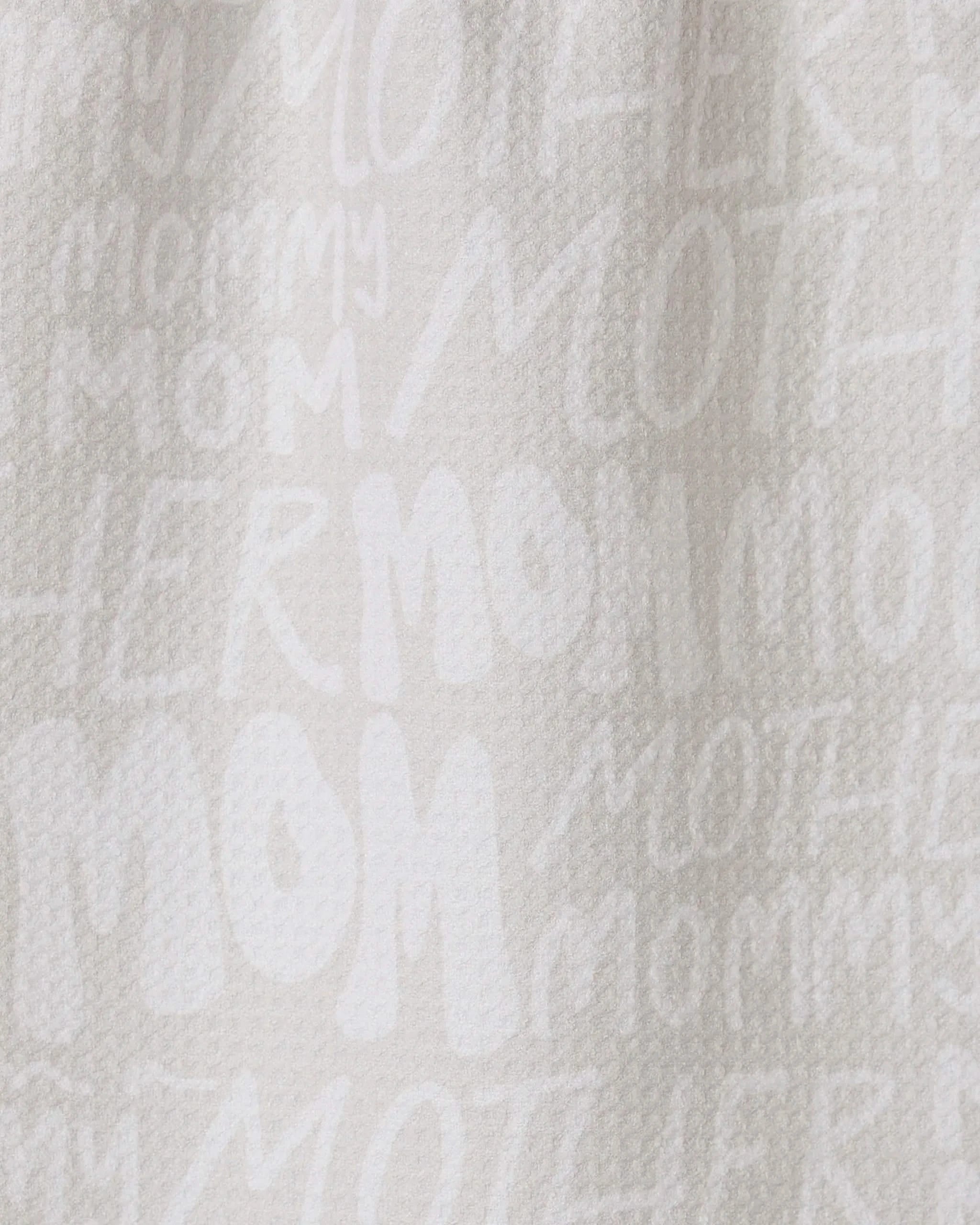 The GEOMETRY Mom bar towel is crafted from recycled white textured fabric, featuring “MOM,” “MOTHER,” and “MOMMY” in varied fonts and sizes printed subtly across its surface.