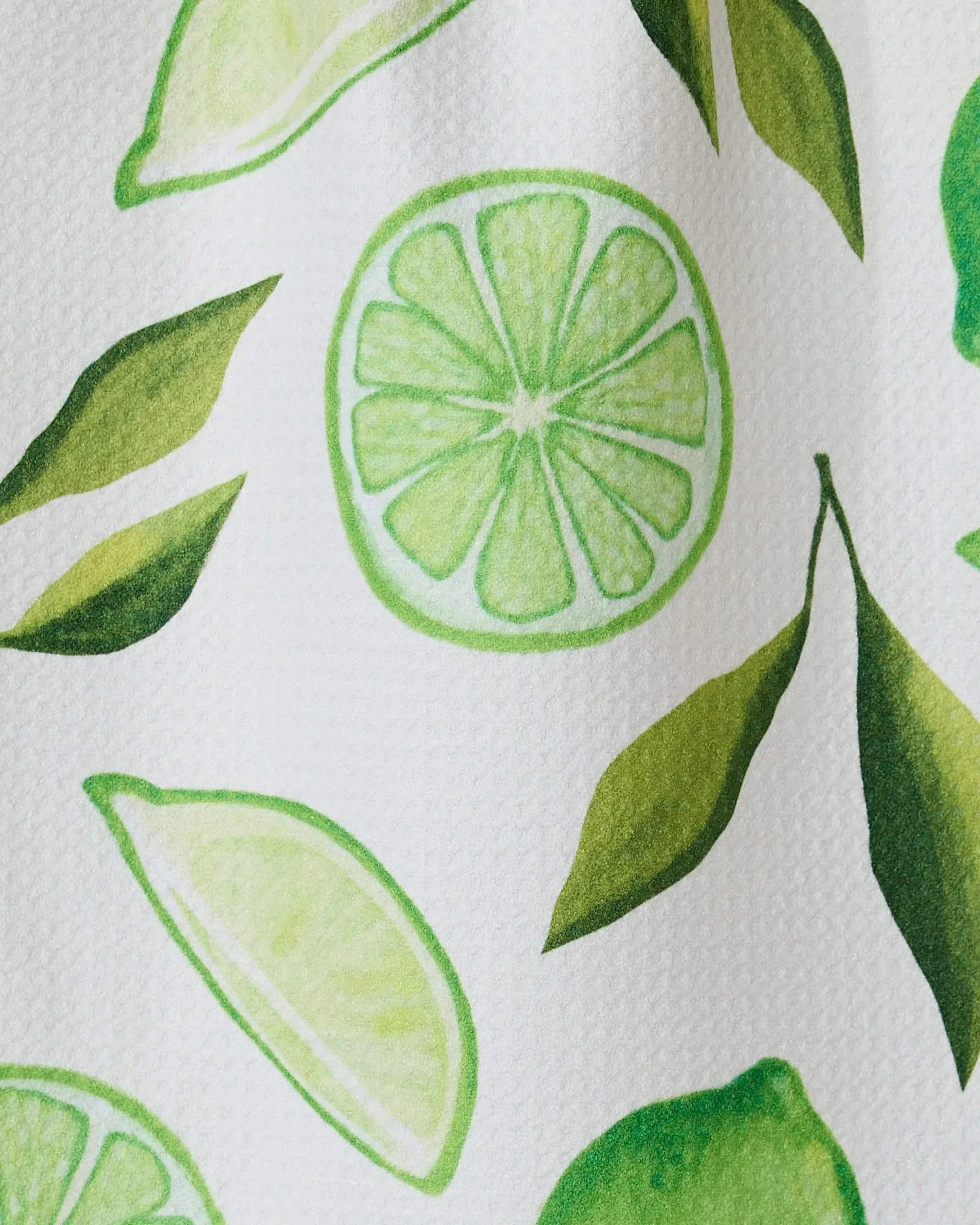 The GEOMETRY Lima bar towel features a bright, fresh pattern of green lime slices, halves, and leaves on soft Geoweave fabric made from recycled materials. The hand-drawn design appears on a white background.