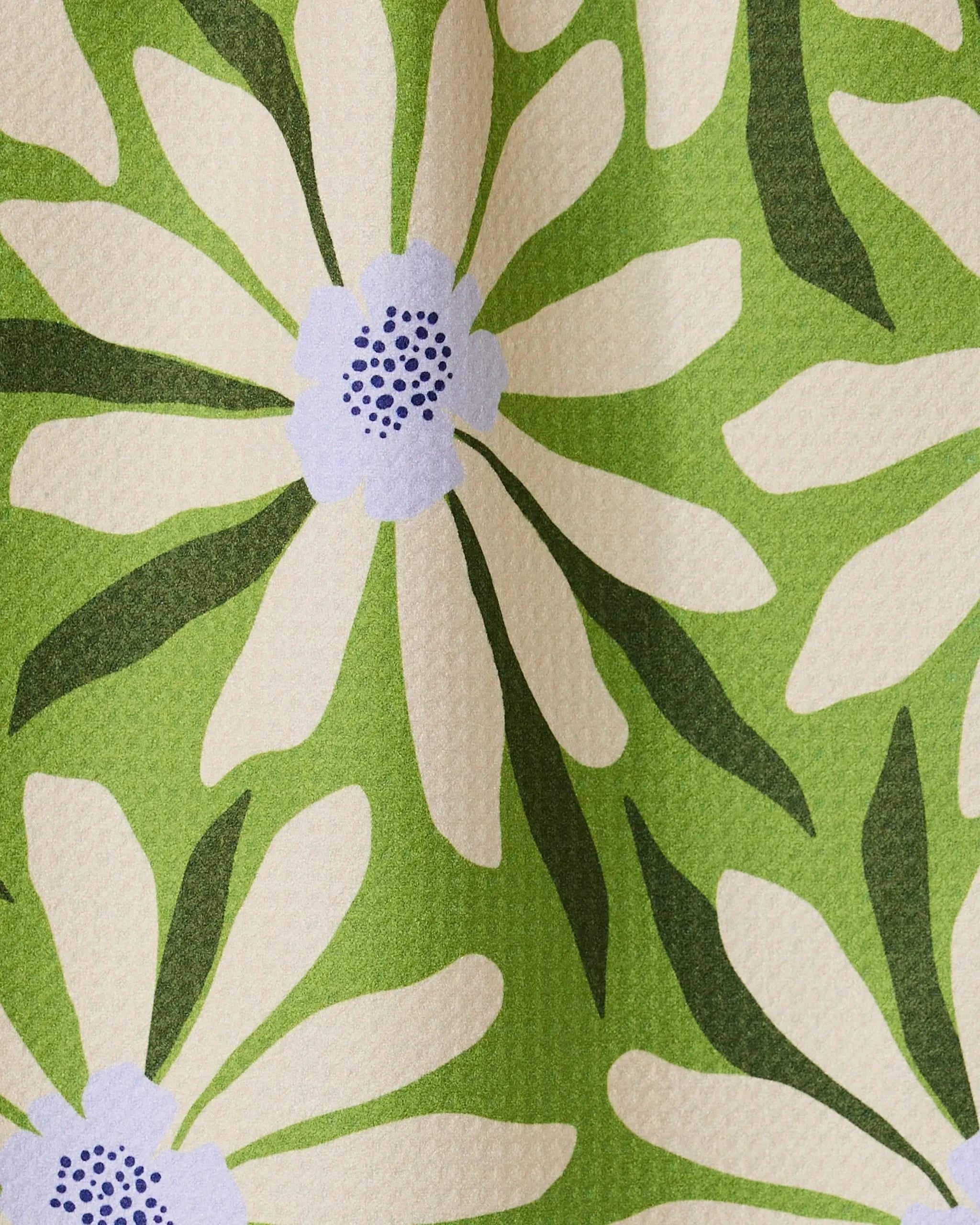 A close-up of the GEOMETRY Bliss and Bloom bar towel shows its ultra-absorbent, textured fabric featuring large white daisies with purple centers and green leaves on a light green background, displayed in soft folds.