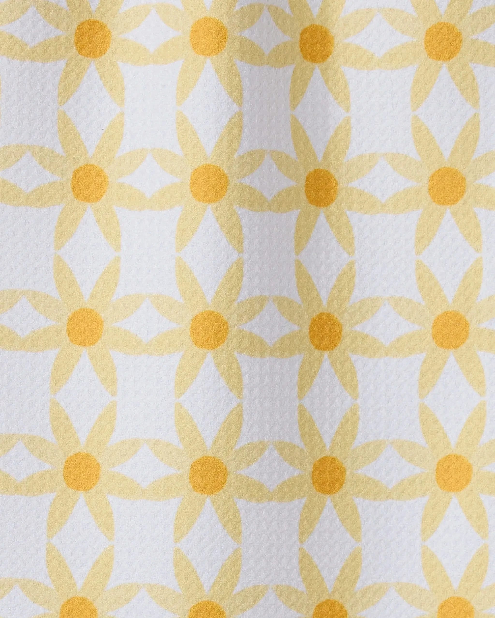 A close-up of GEOMETRYs Daisies recycled kitchen towel, showcasing a repeating yellow daisy-like geometric pattern on a white background.