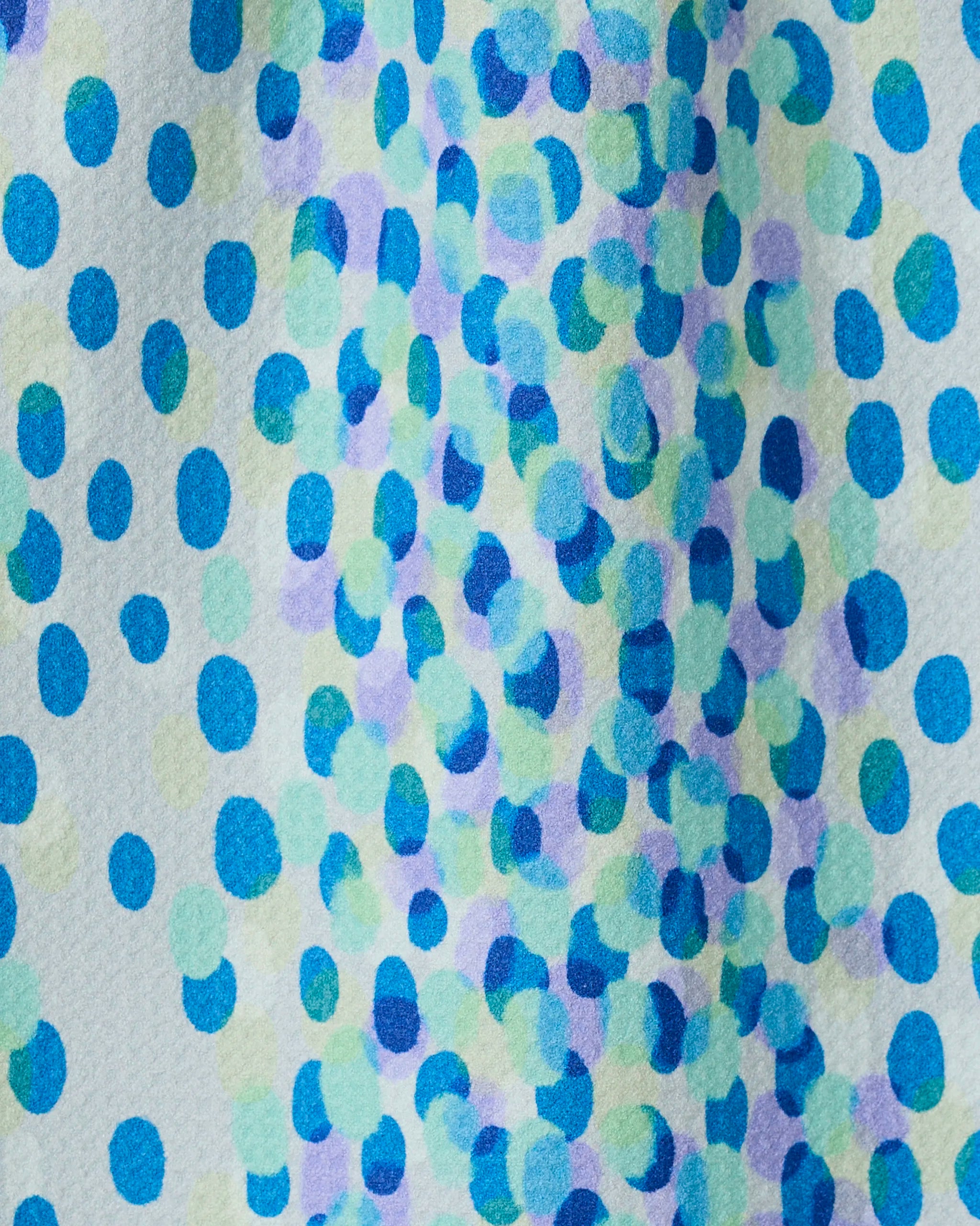 A close-up of Spotty Summer by GEOMETRY shows a vibrant, abstract bar towel made from recycled materials, featuring blue, green, and purple dots scattered across a white background.