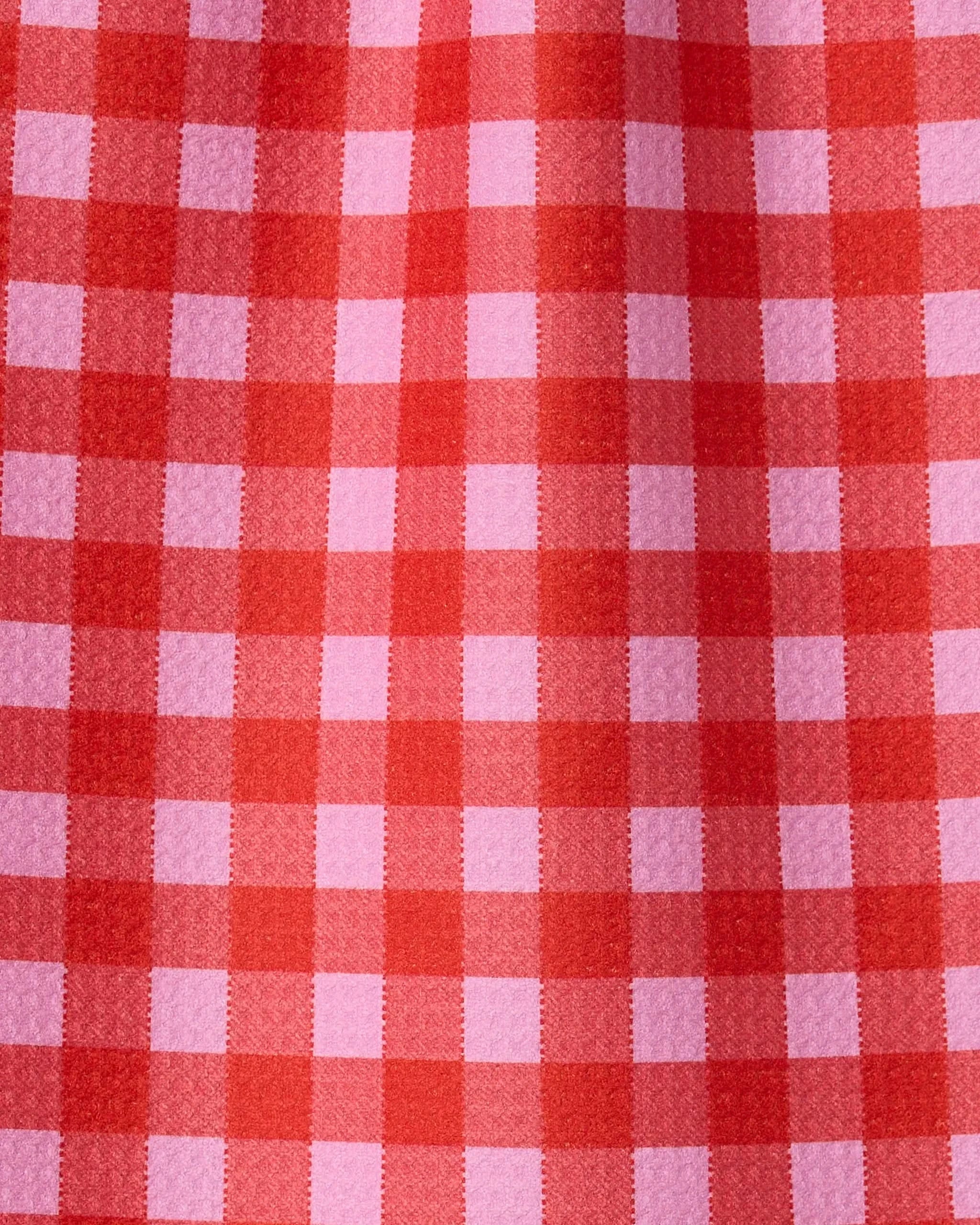Close-up of Cherry Gingham by GEOMETRY, featuring a red and pink checkered pattern with visible texture, crafted from recycled materials and highlighted by fabric folds.