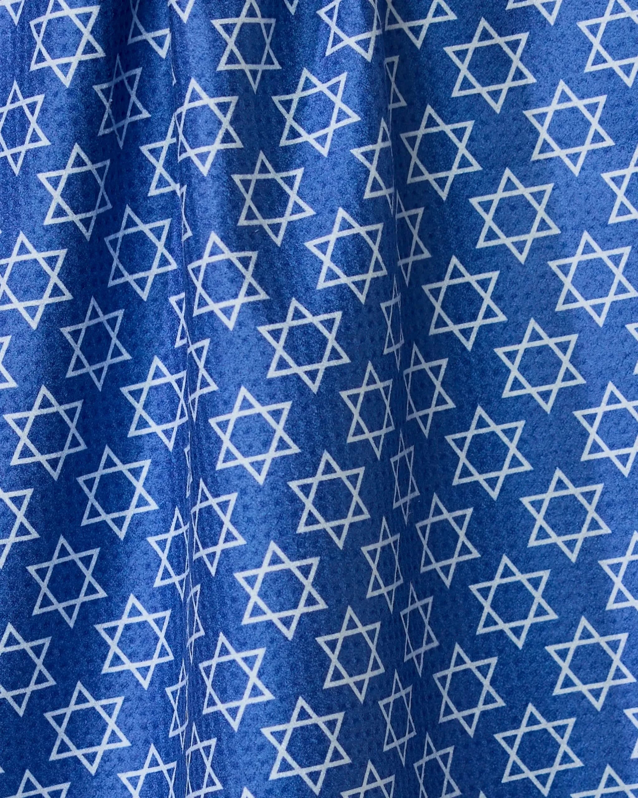 A blue double-sided tea towel from Geometry, called Star Of David, featuring an even pattern of white Stars of David. The fabrics folds and creases create varied light and shadow across the surface.